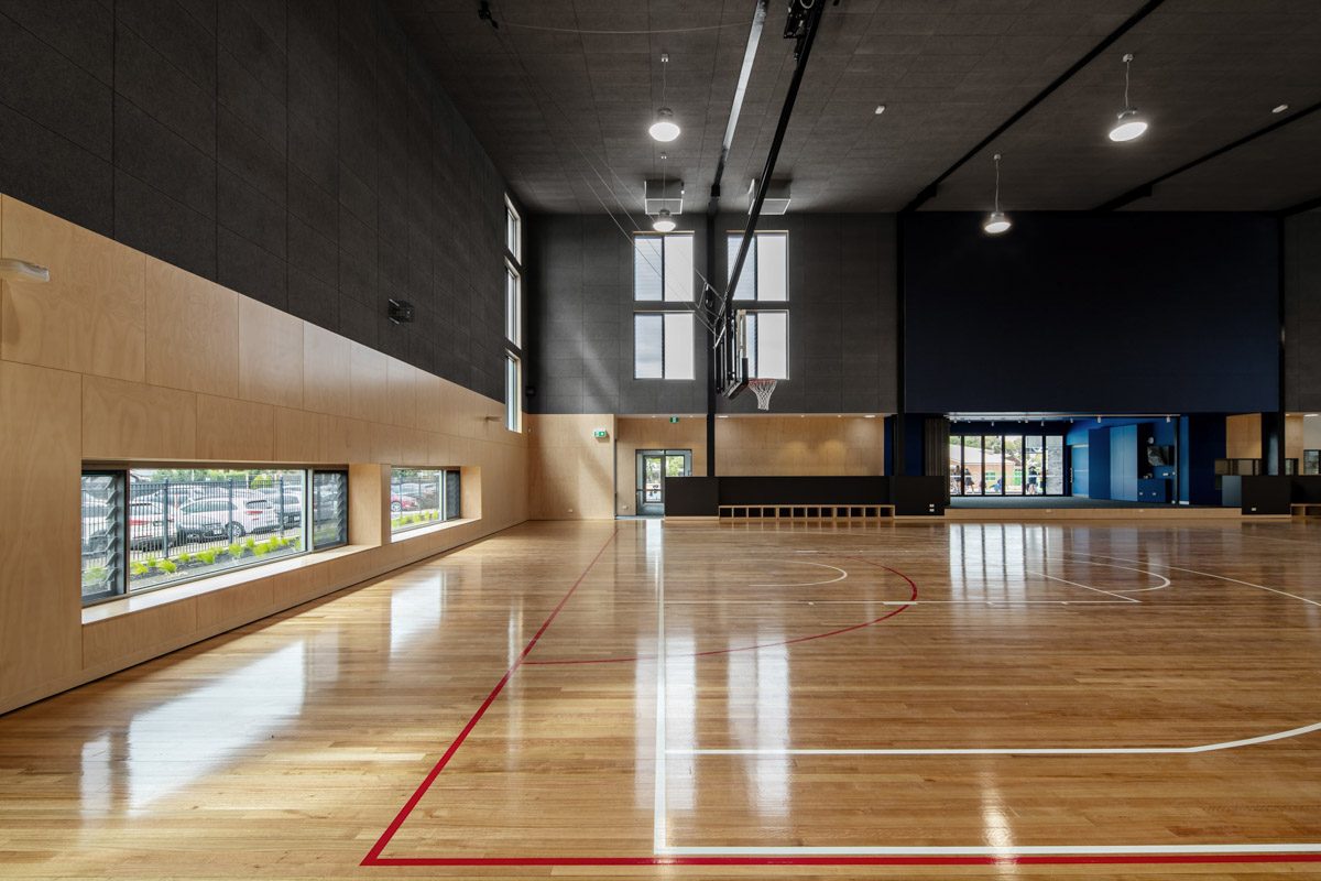 An indoor sports court with polished timber flooring, high ceilings, and large windows. Basketball hoops are mounted, and natural light fills the space.