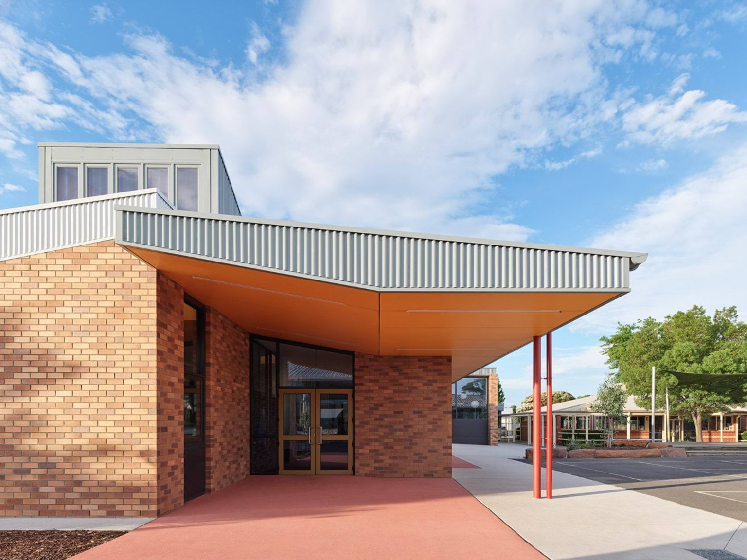 Close-up of school entrance with brick walls, orange canopy underside, and red support columns.