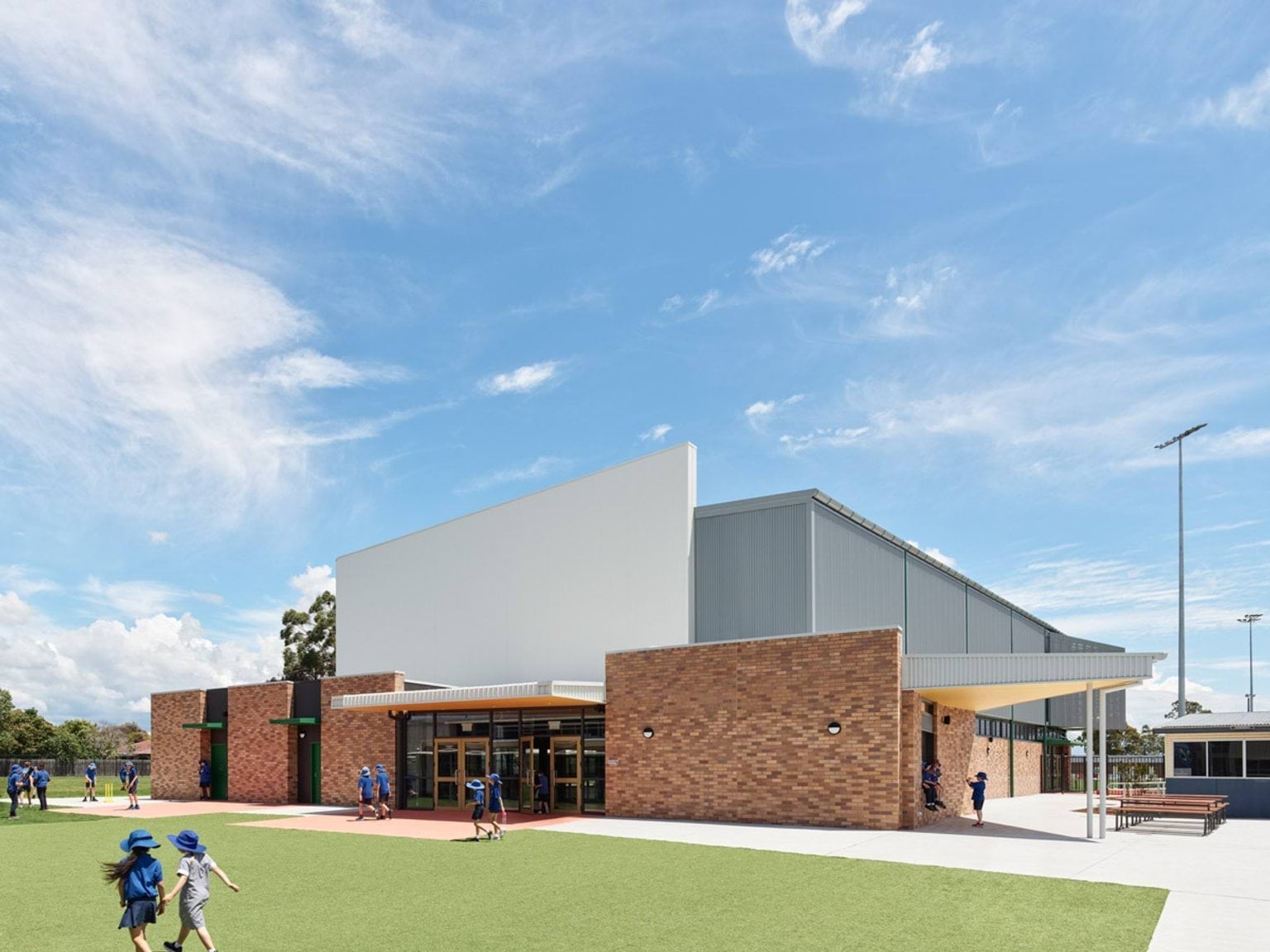 Students playing near a brick and white school hall with covered outdoor seating area.