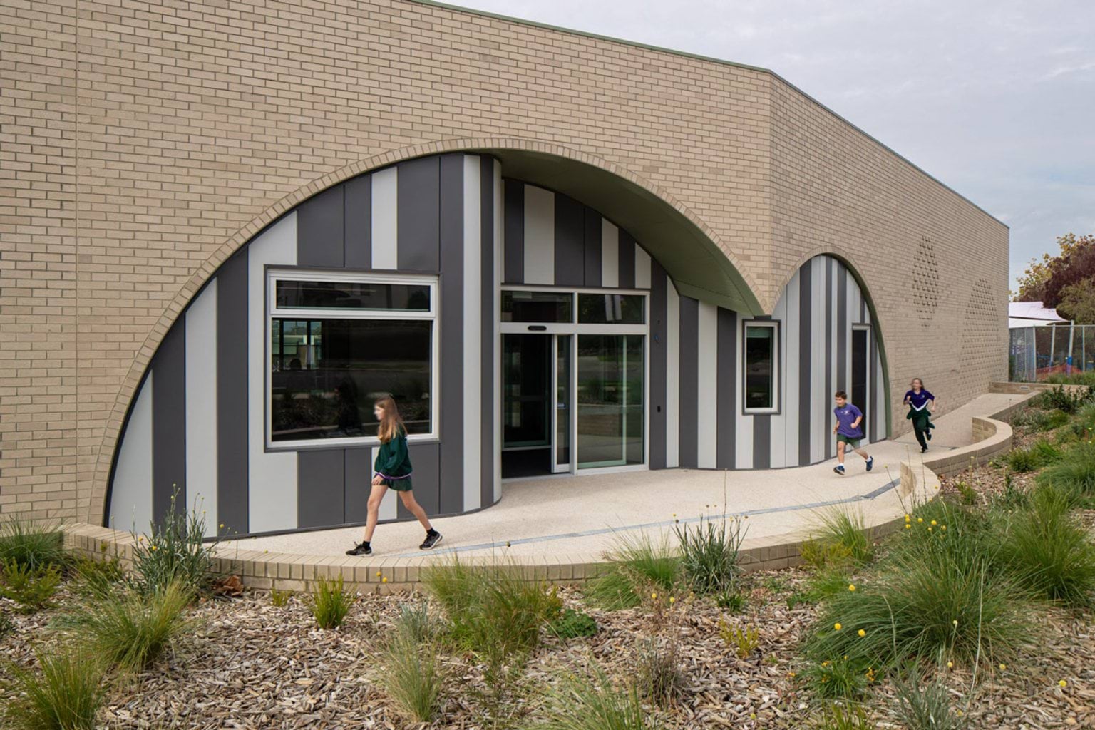 School entrance with striped cladding and arched brickwork, surrounded by native garden landscaping.