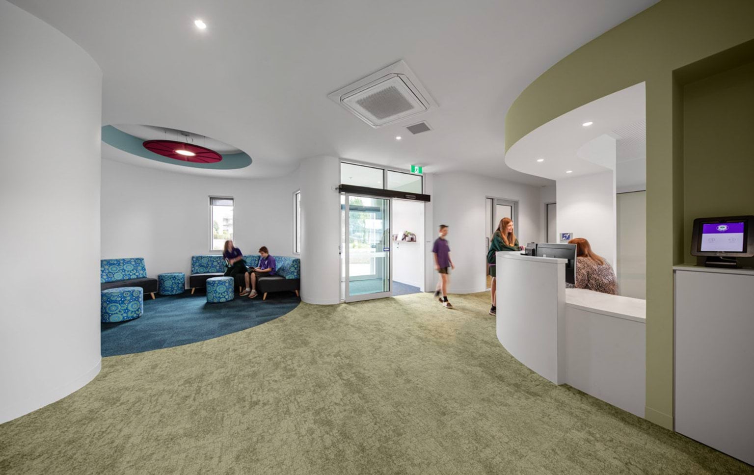 Bright school reception area with curved walls, patterned seating, and a front desk near the entrance.