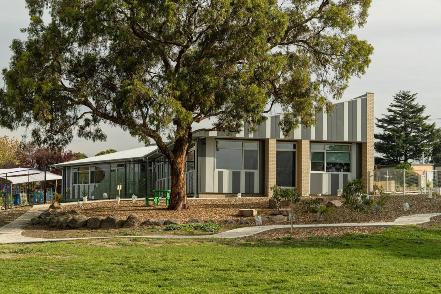 School building with striped cladding and large windows, set among trees and landscaped outdoor spaces.