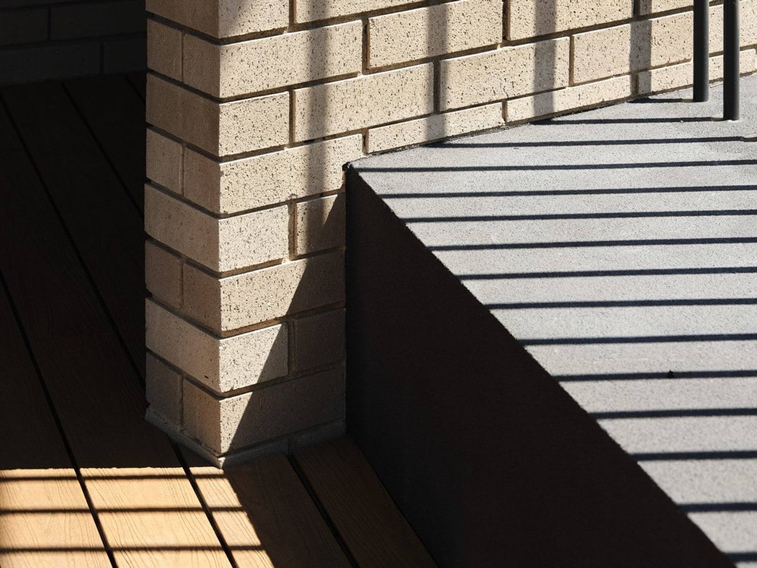 The outdoor play area with timber decking, green play mats and garden beds. The kindergarten building curves around the space with cream brick walls and a dark roof.
