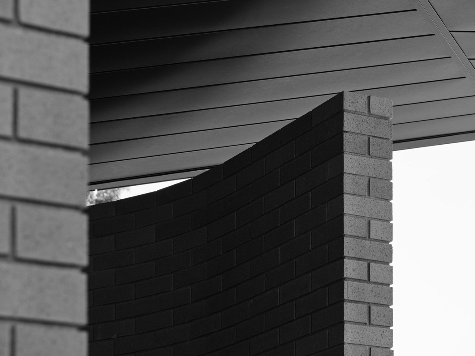 A close-up of the kindergarten’s curved brick wall and dark roof panels, showing the architectural detail in black and white.