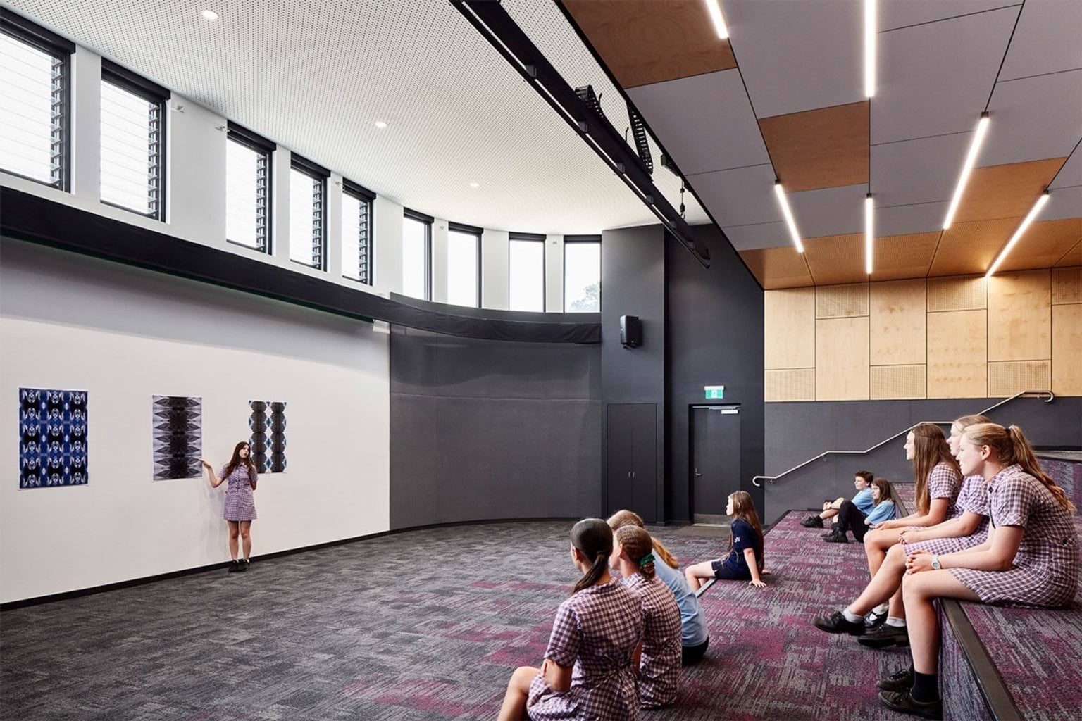 Tiered learning space with curved seating and carpeted steps, students sitting and viewing artwork displayed on wall