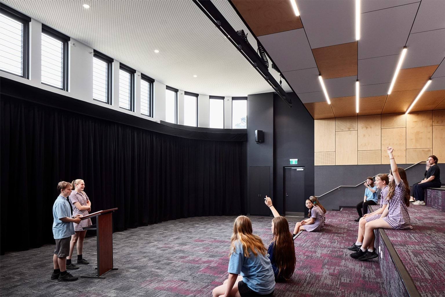 Tiered presentation space with black curtain backdrop, podium and students seated on carpeted steps participating in discussion