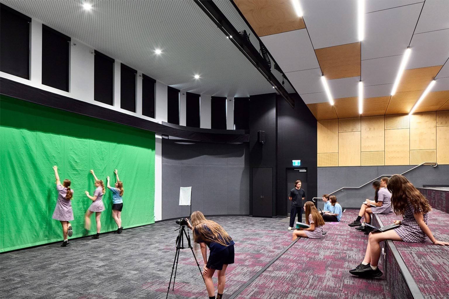 Green screen backdrop, camera on tripod and students preparing for filming while others observe