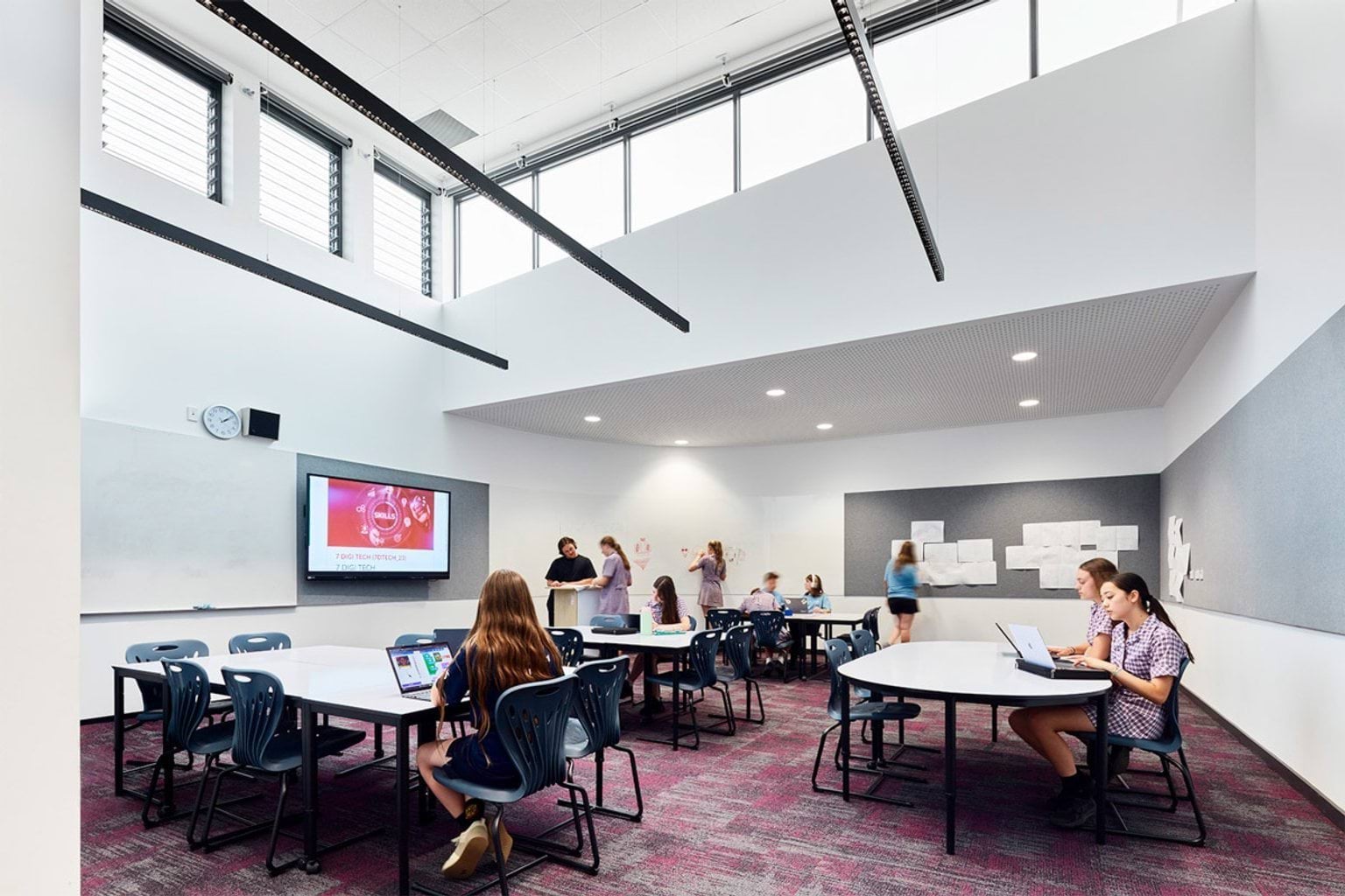 Collaborative classroom with big tables, large windows and students working on laptops and writing on whiteboards