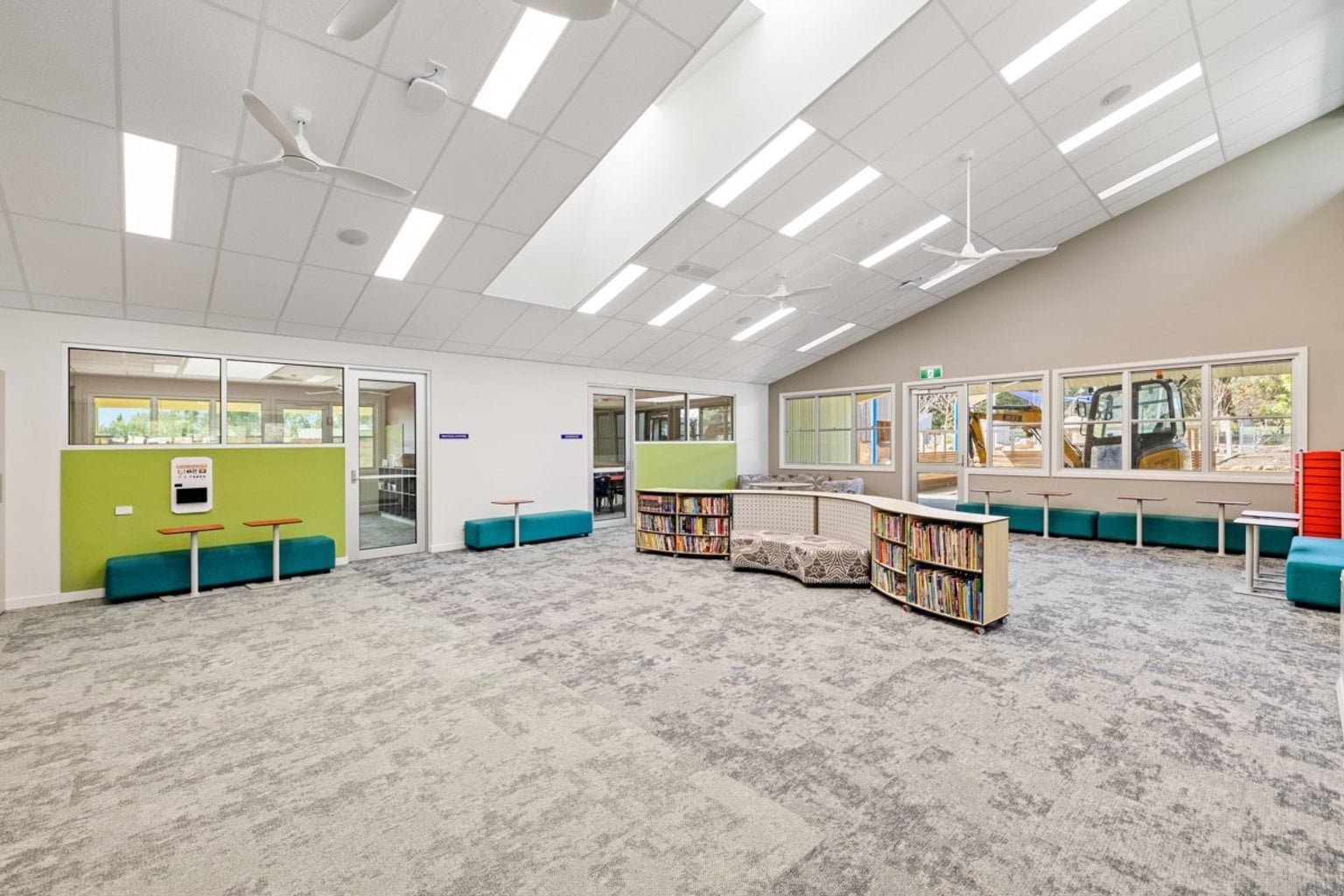 A large library space with curved shelving, teal seating, and bright overhead lighting. Windows line one wall.