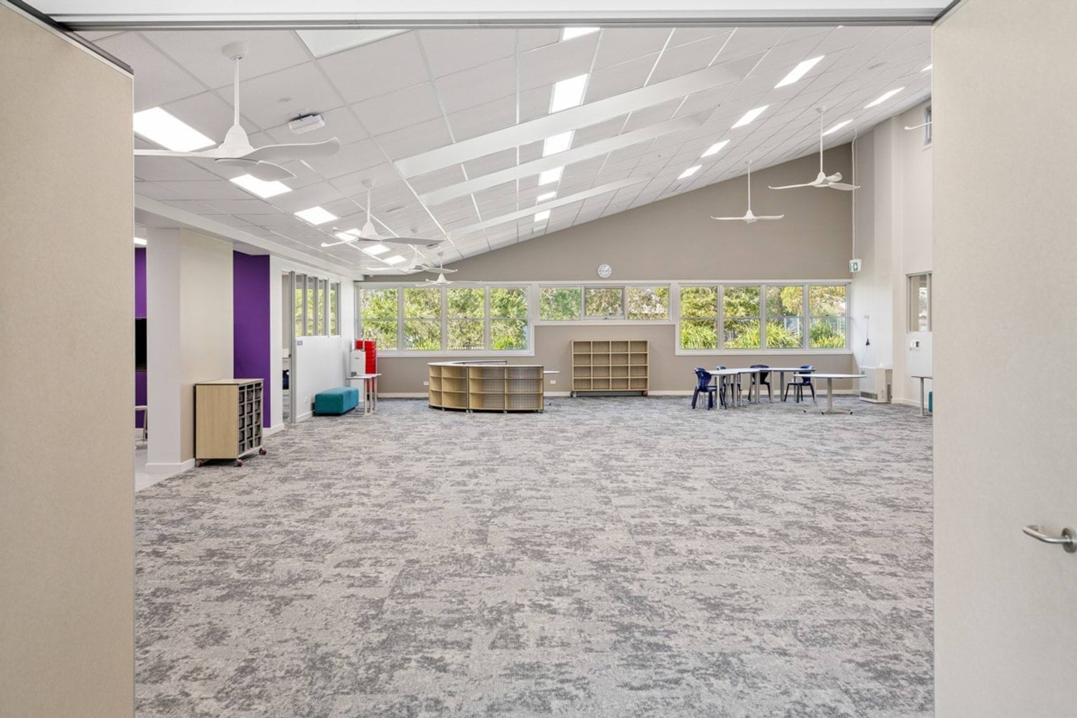 A large library space with curved shelving, teal seating, and bright overhead lighting. Windows line one wall.