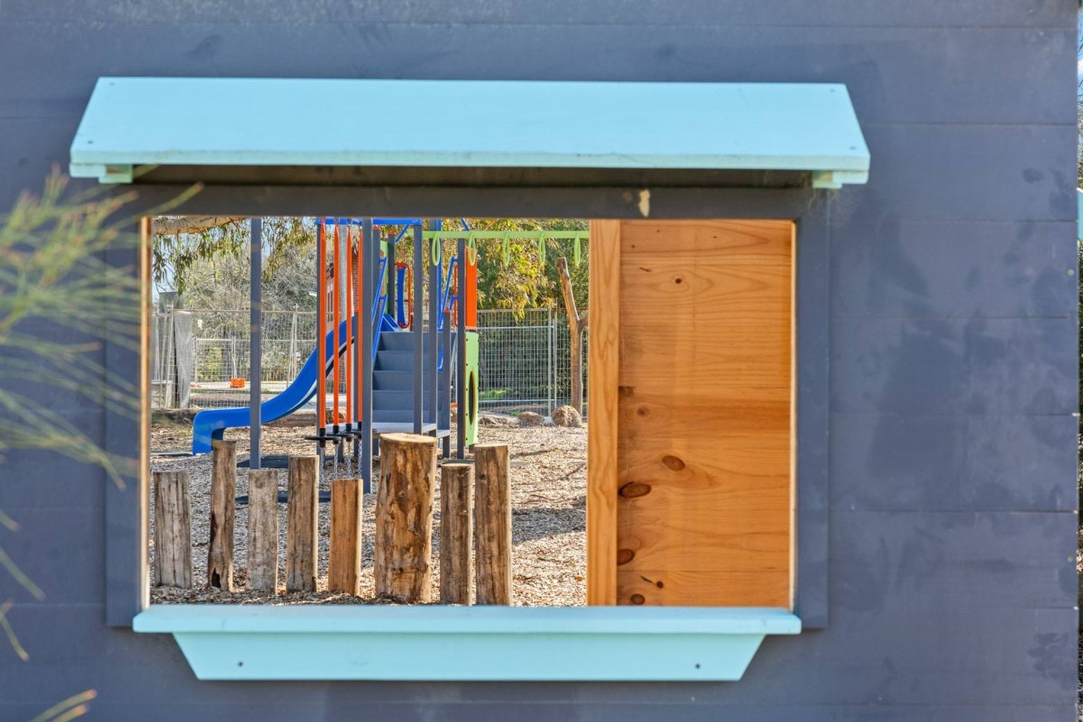 A view of playground equipment through a timber-framed window in a small playhouse.