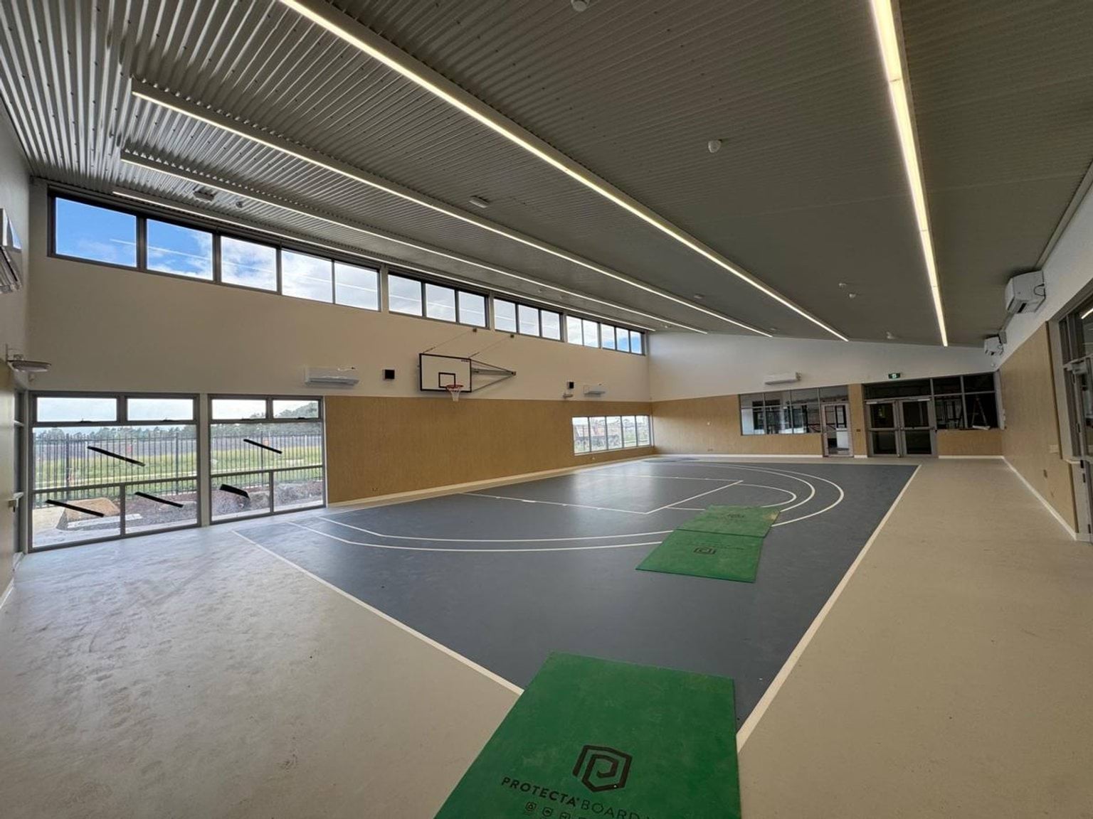 Indoor basketball court under construction. The court is blue and there are windows facing outside.
