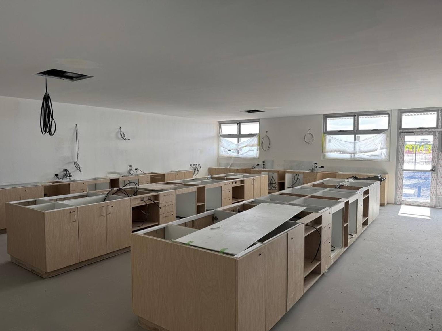 Classroom under construction. There are benches in different states of assembly and cables in the ceiling. 