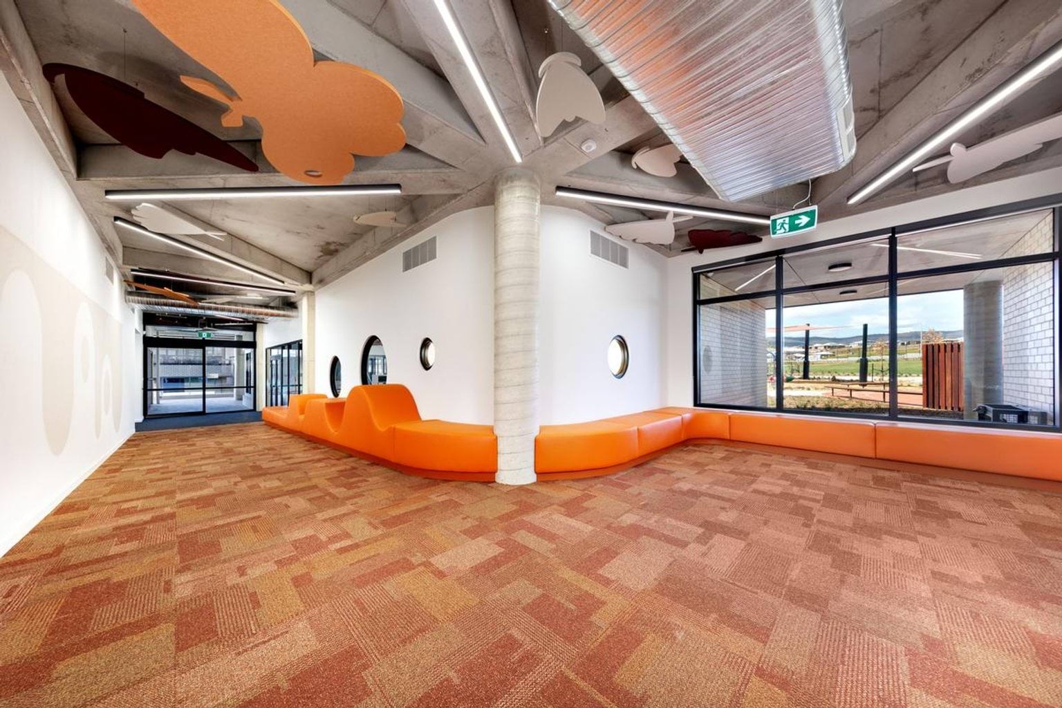 Inside the new Kerribana Primary School. The room has orange carpet and orange bench seating wrapping around the wall. There is a large orange butterfly design suspended from the ceiling.