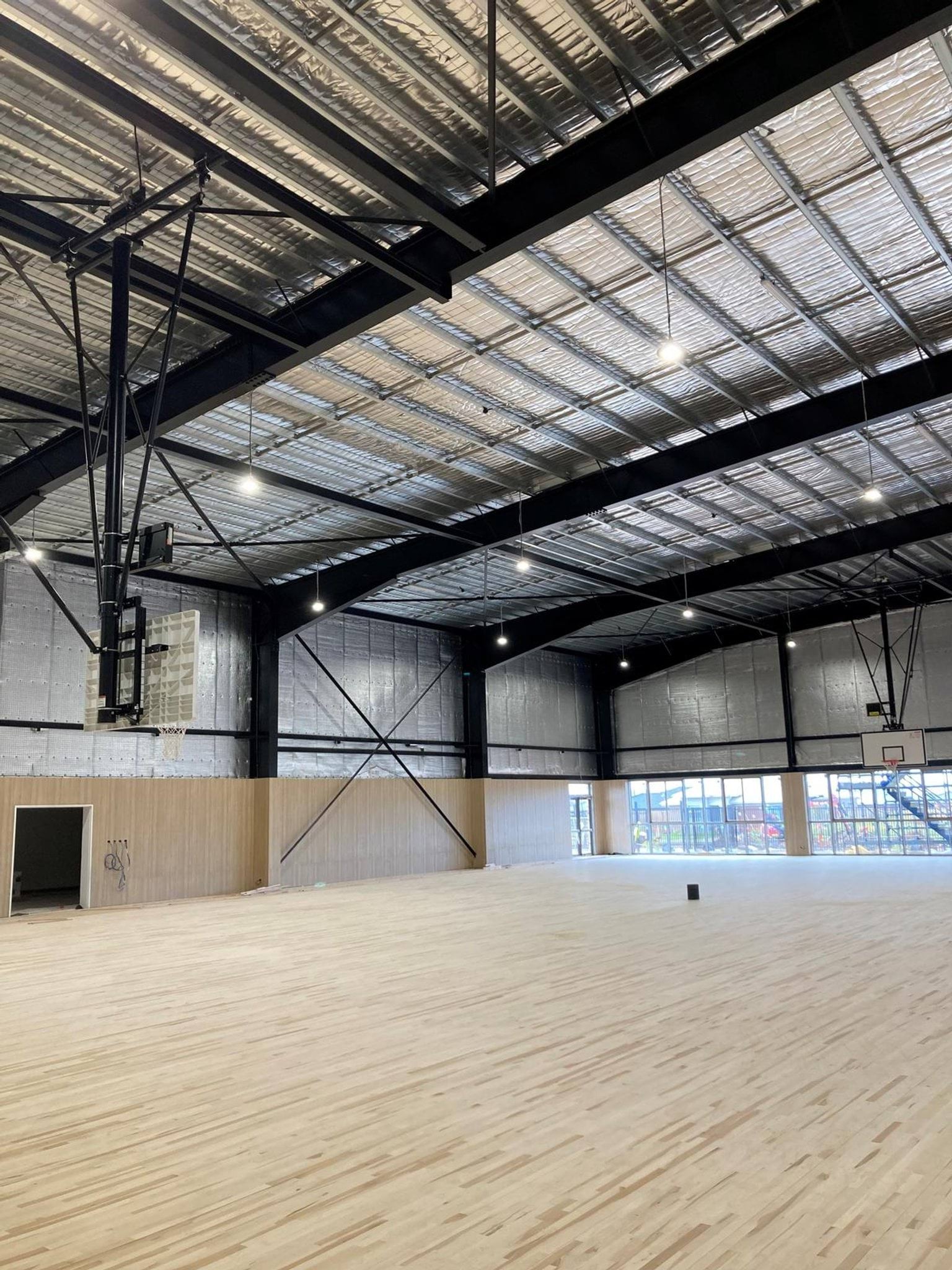 Indoor gym with basketball hoops, wood flooring, and silver insulation in the roof