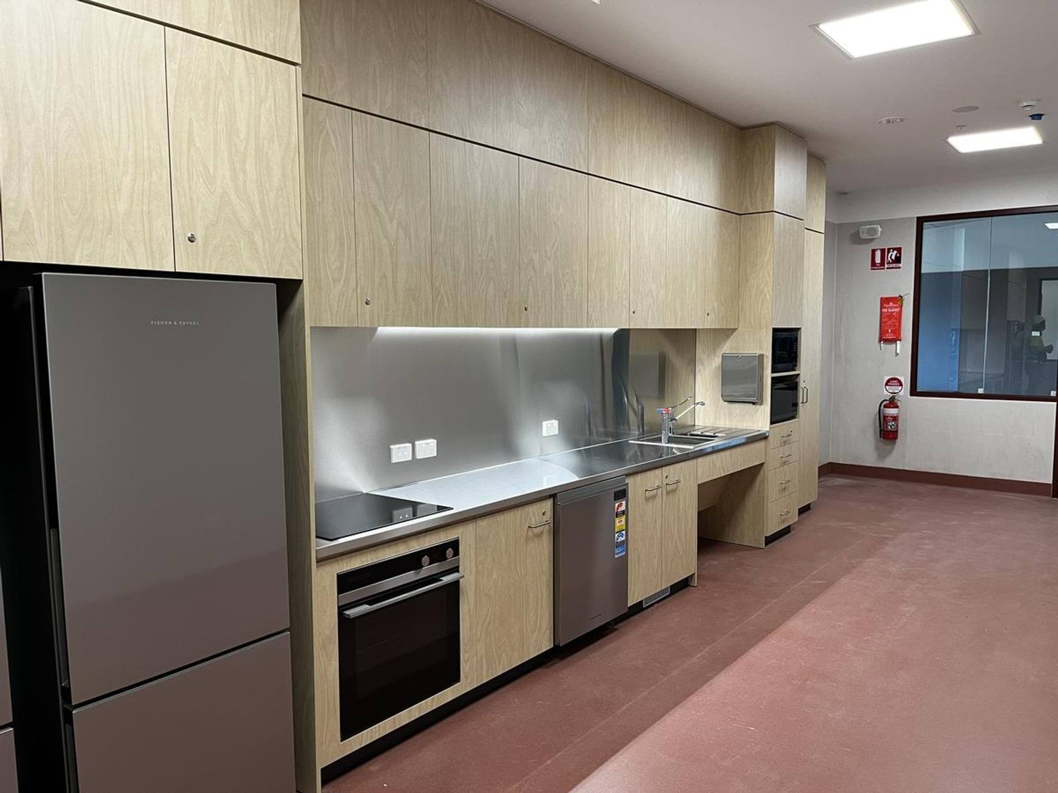 A modern kitchen with timber cabinetry, stainless steel benchtops, and appliances including an oven, dishwasher, and fridge.