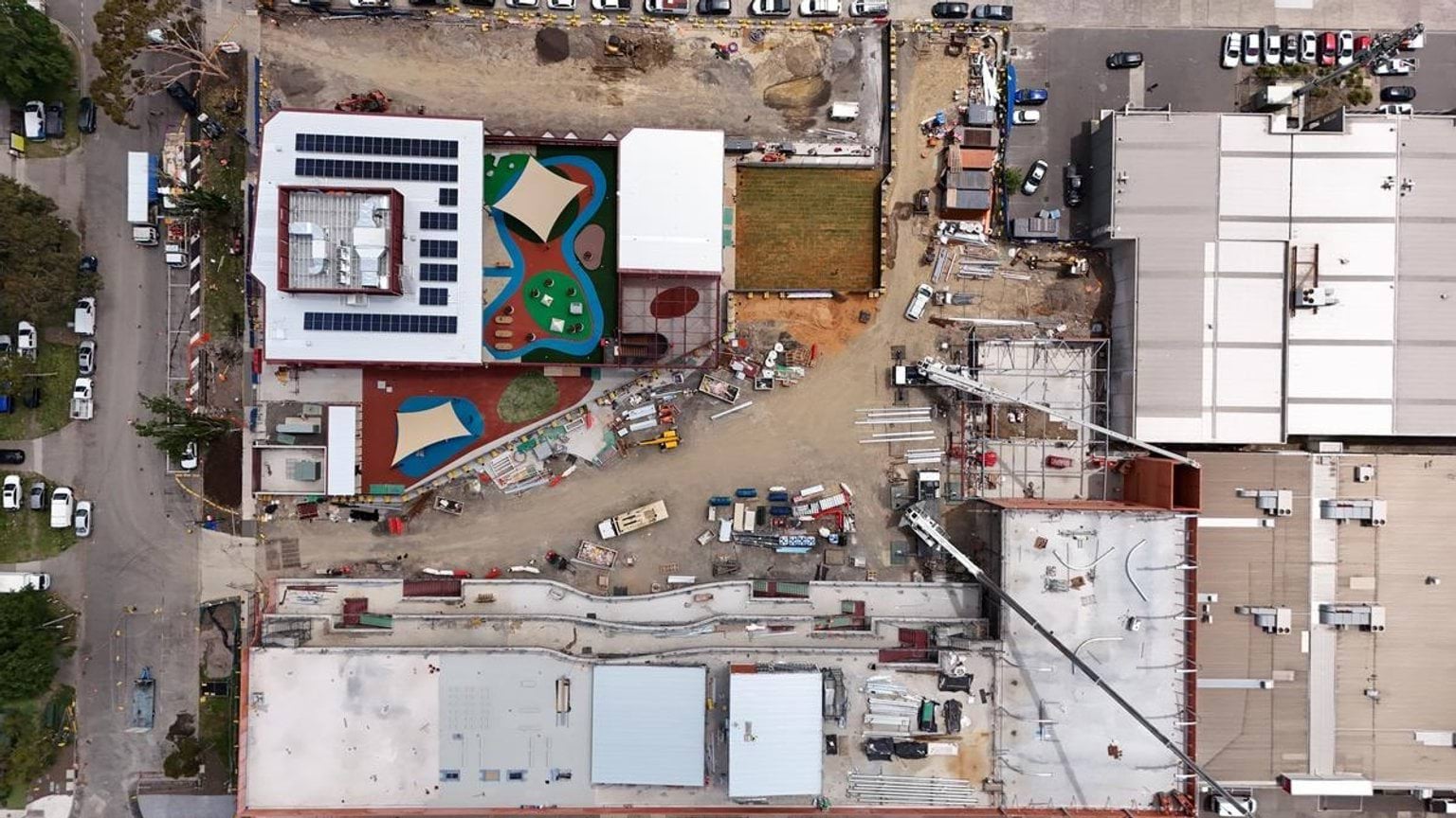 An overhead view of the kindergarten and school site under construction, showing buildings with solar panels and colourful outdoor play zones.