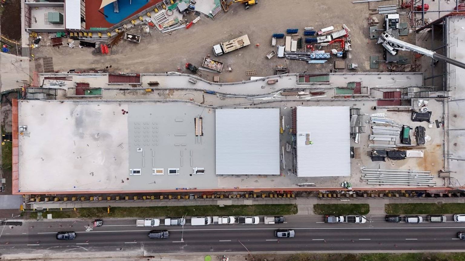 An overhead view of the school buildings with flat roofs, construction materials, and vehicles lined along the street.