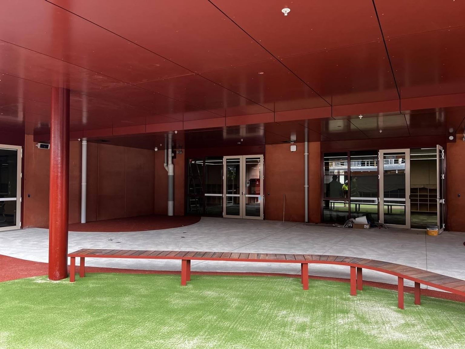 A partially completed outdoor courtyard with green artificial turf, curved seating, and red walls surrounding the area.