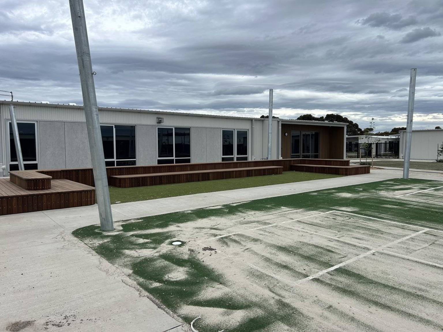 A courtyard with timber seating platforms and artificial turf in front of a modern school building with large windows.