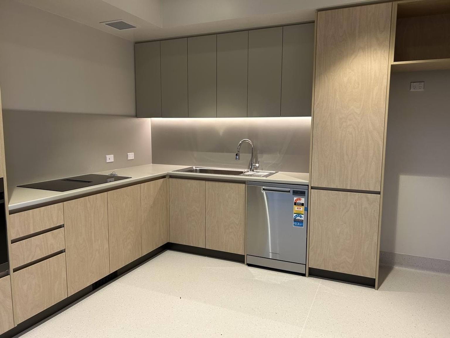 A modern kitchen with timber cabinetry, stainless steel appliances, and a light-coloured benchtop in an L-shaped layout.