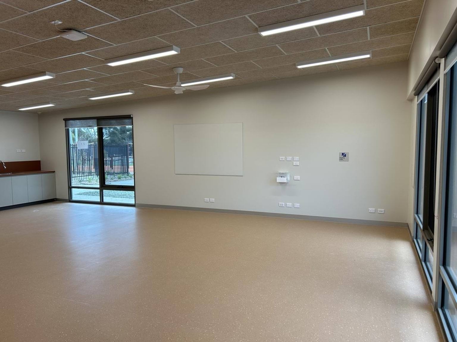A spacious classroom with light flooring, large windows, and built-in cabinetry along the walls under bright ceiling lights.
