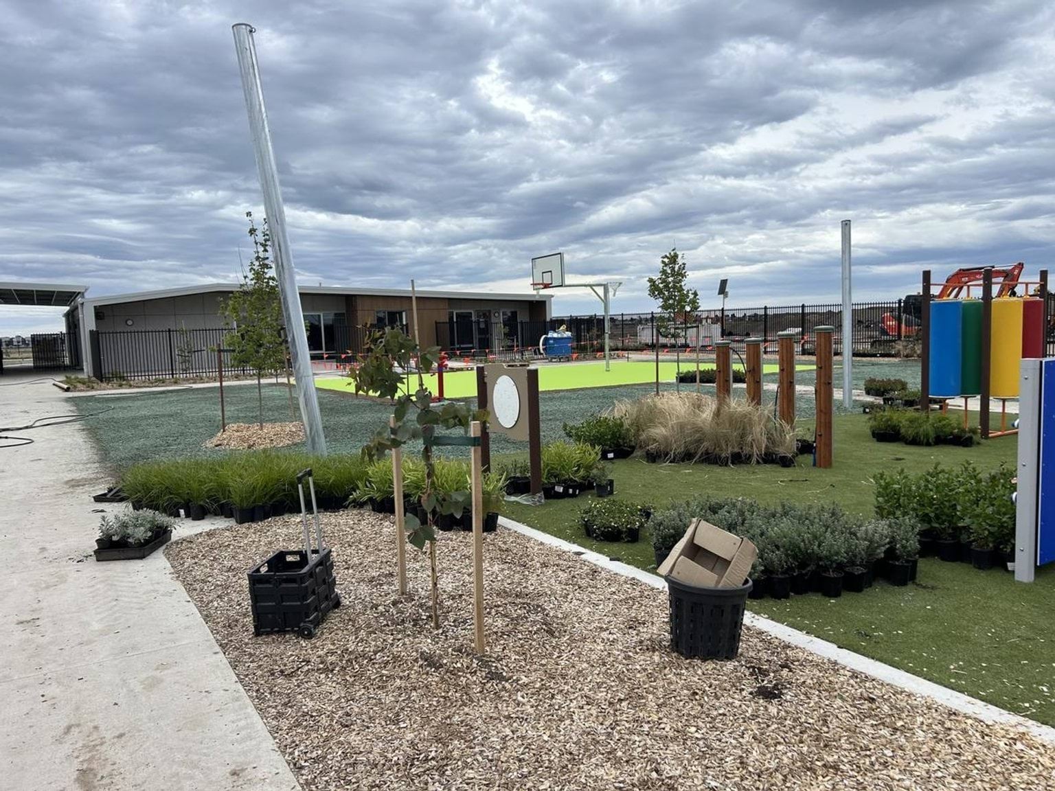 An outdoor play area with climbing equipment, basketball hoop, and landscaped garden beds with plants ready for planting.