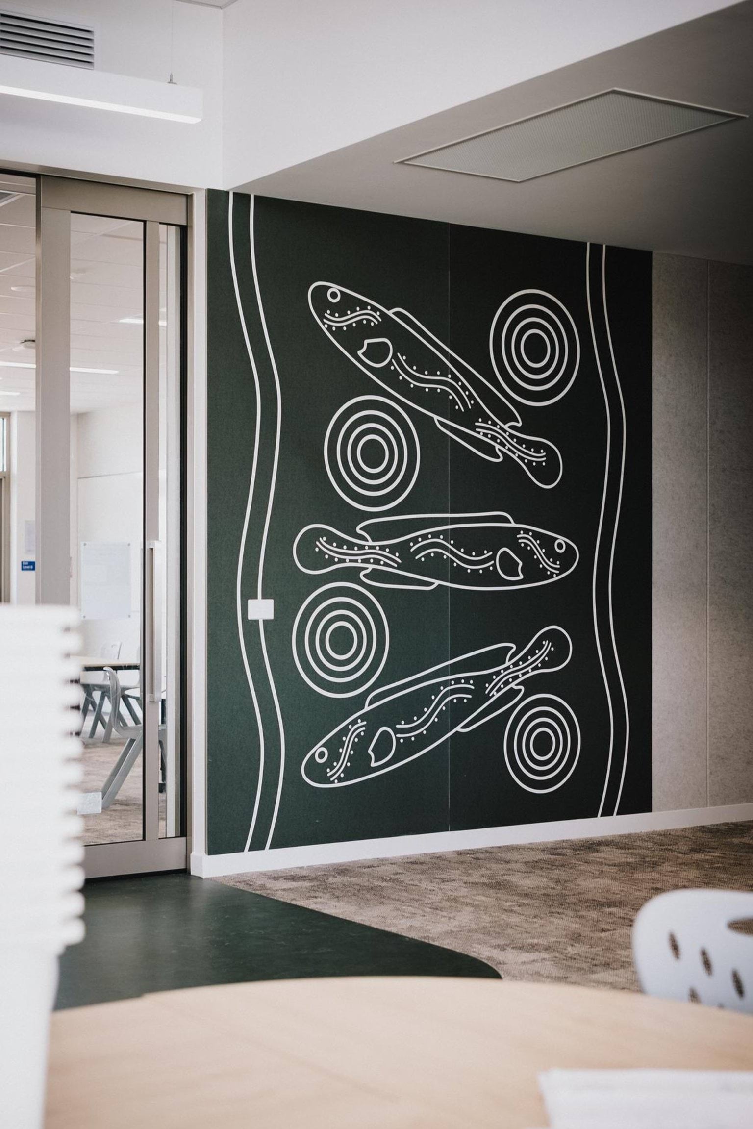 Interior classroom wall featuring Aboriginal artwork with fish and circular patterns in white on a dark green background