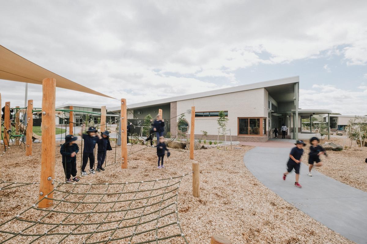 Playground with timber climbing structures and soft-fall mulch, with children playing and running nearby