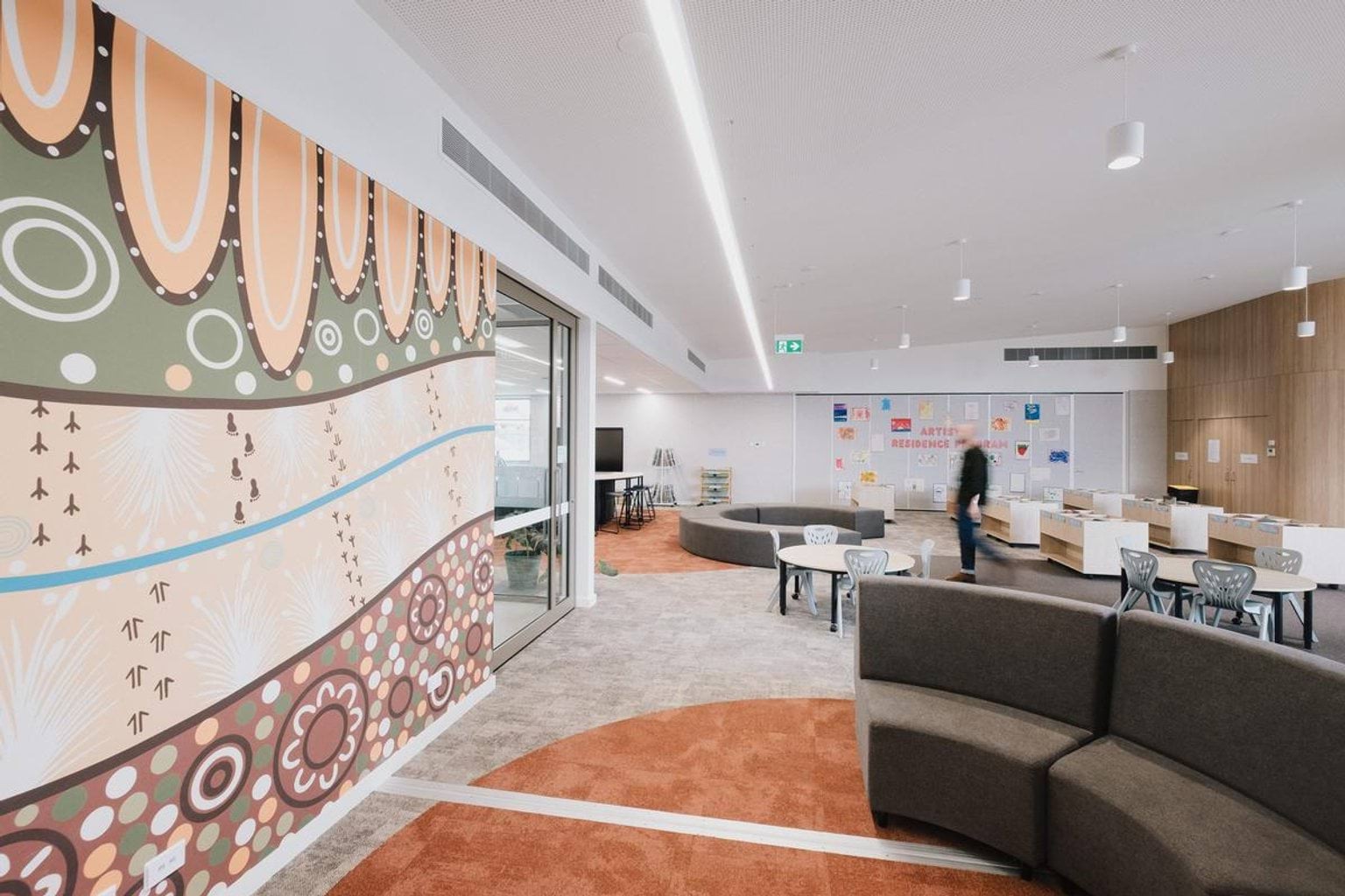 Open learning space with curved seating, colourful feature wall artwork and an adult walking through