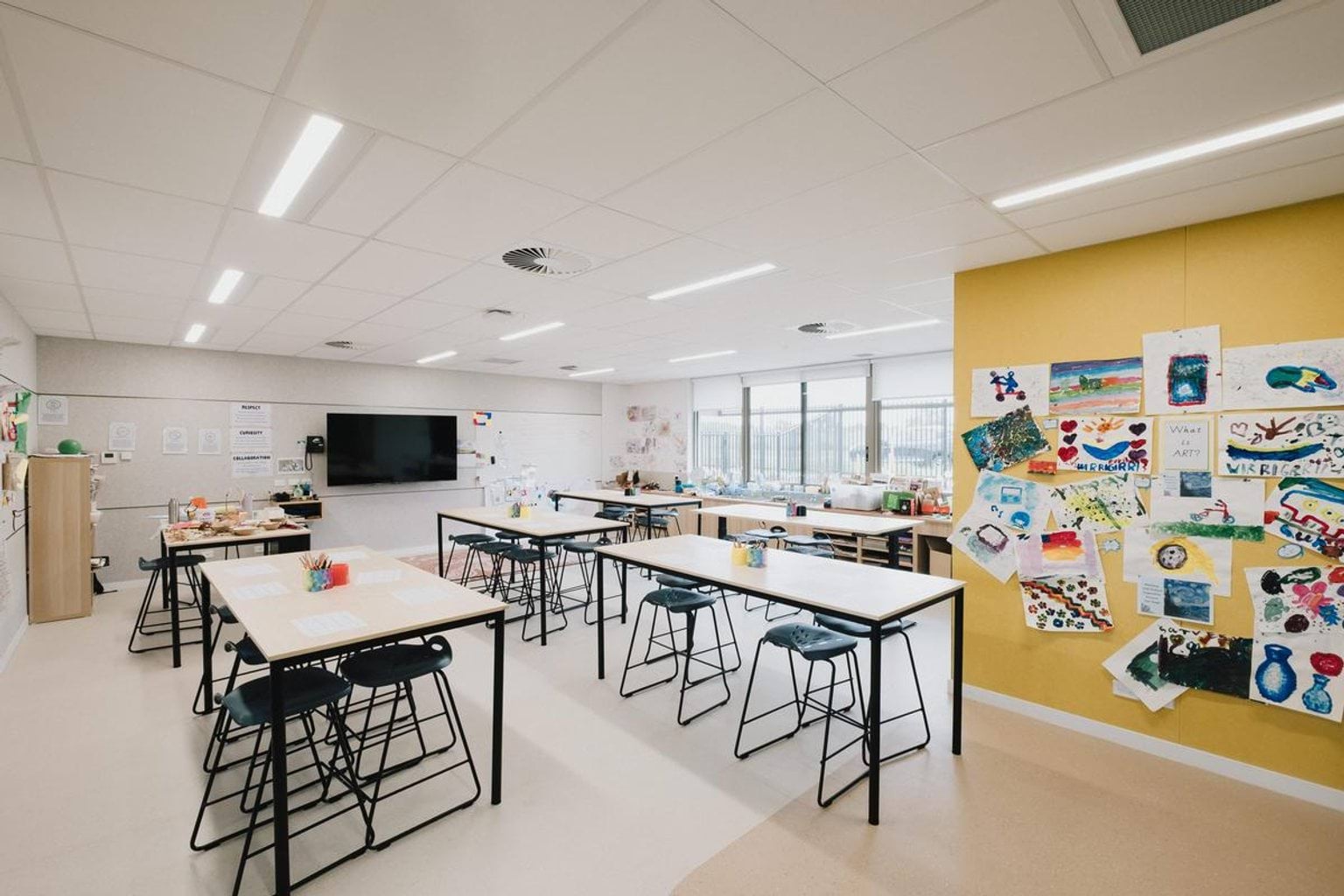 Classroom with high tables, stools, bright yellow feature wall and student artwork displayed