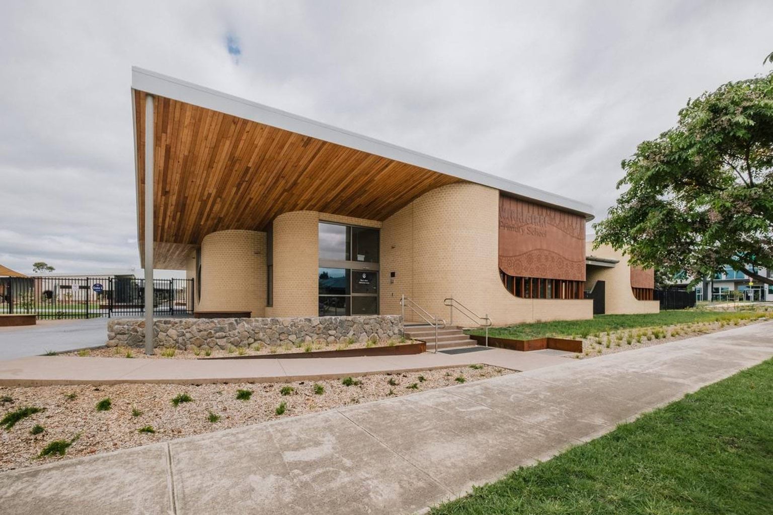 School entrance with curved brick walls, timber soffit and landscaped frontage along footpath