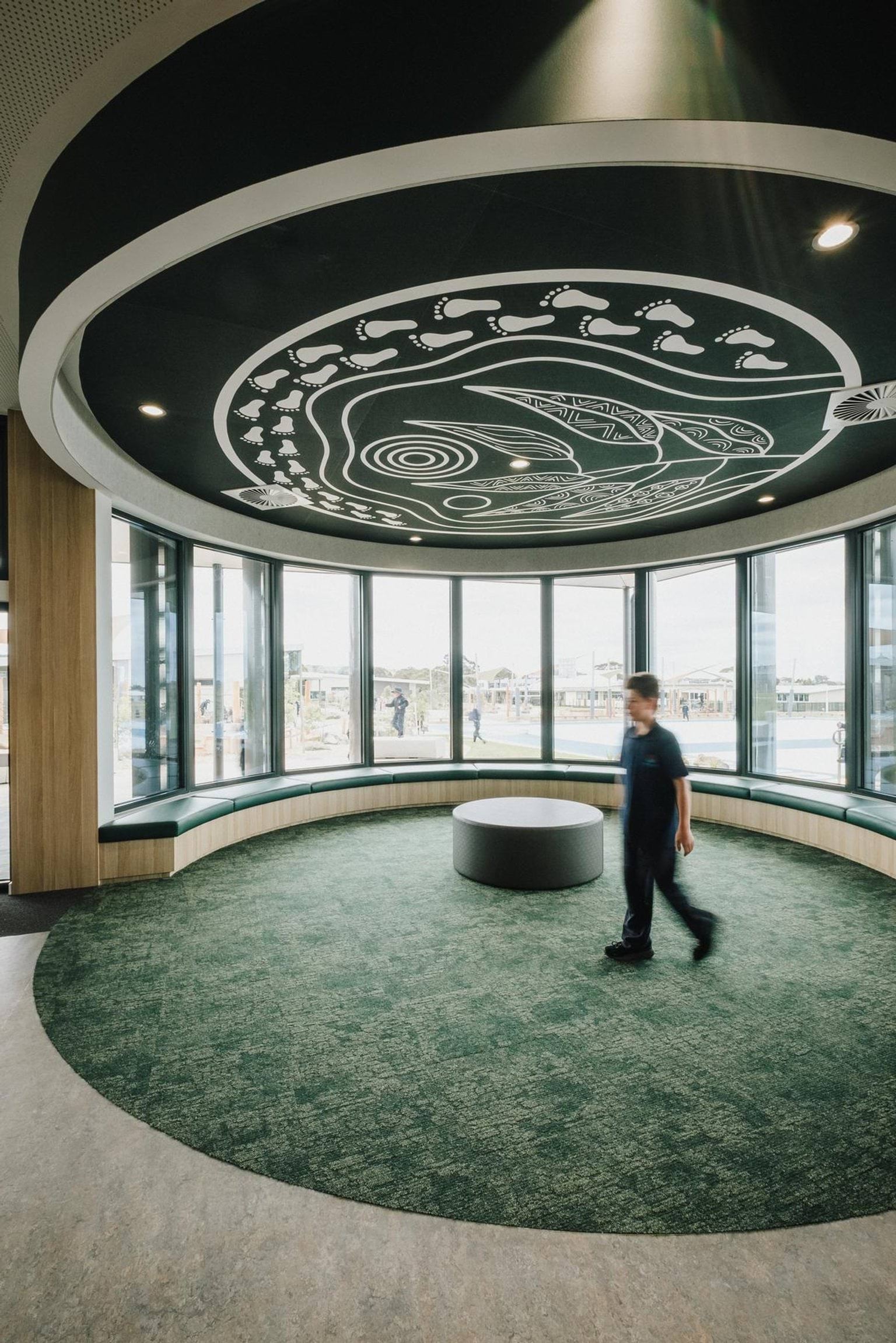 Circular indoor space with patterned ceiling feature and wraparound windows, with a student walking through