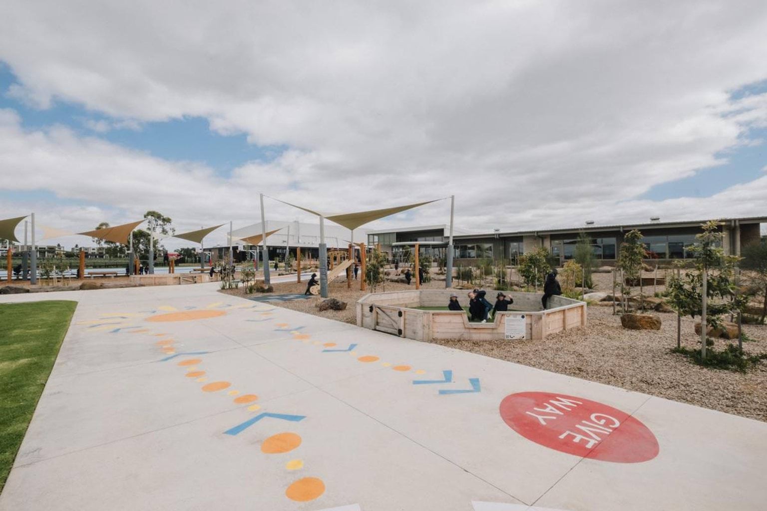 Outdoor learning and play area with shade structures and seating, with students gathered near garden beds