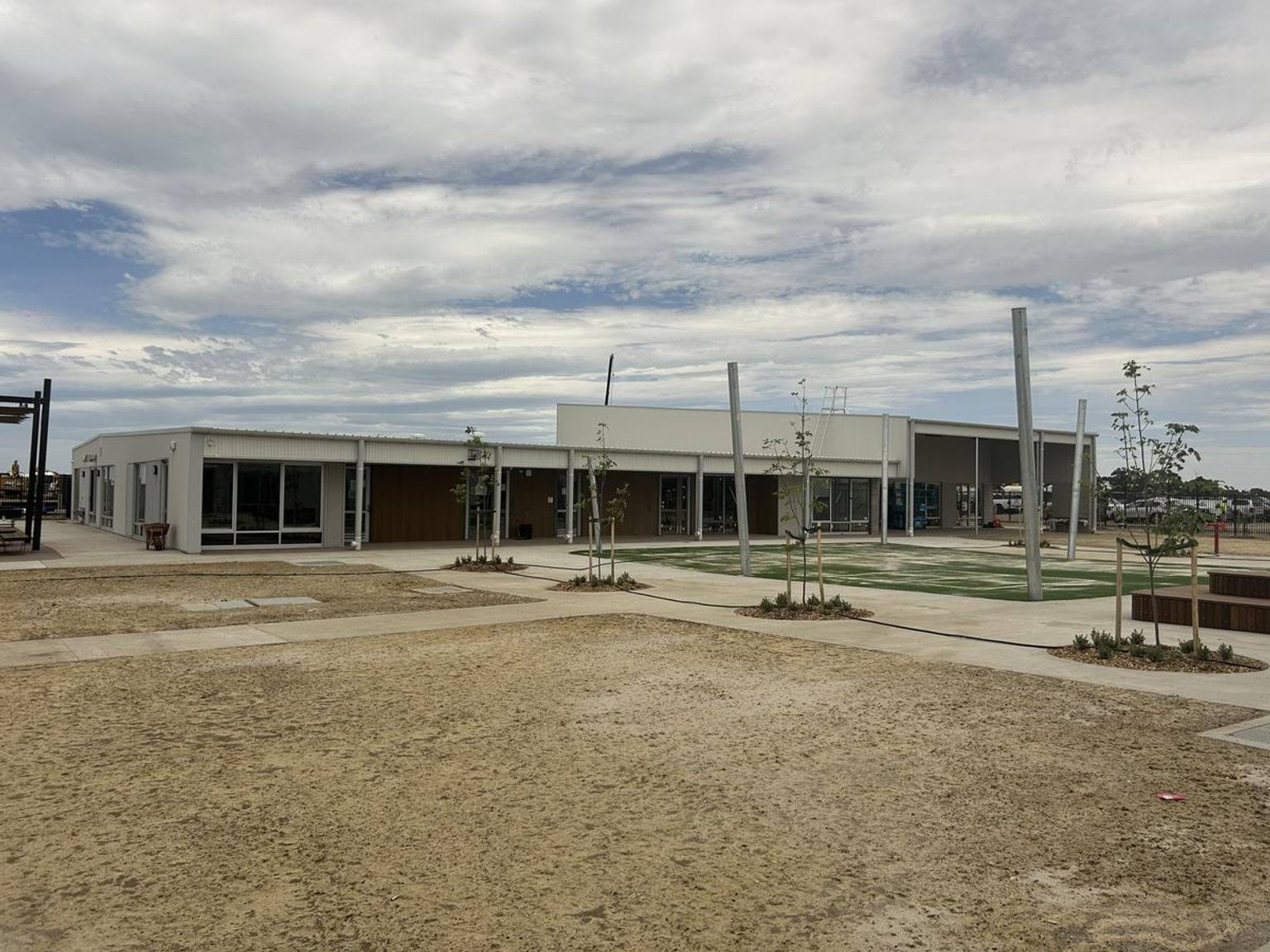 The exterior of a single-storey school building with white walls and large windows, set against a partly cloudy sky.