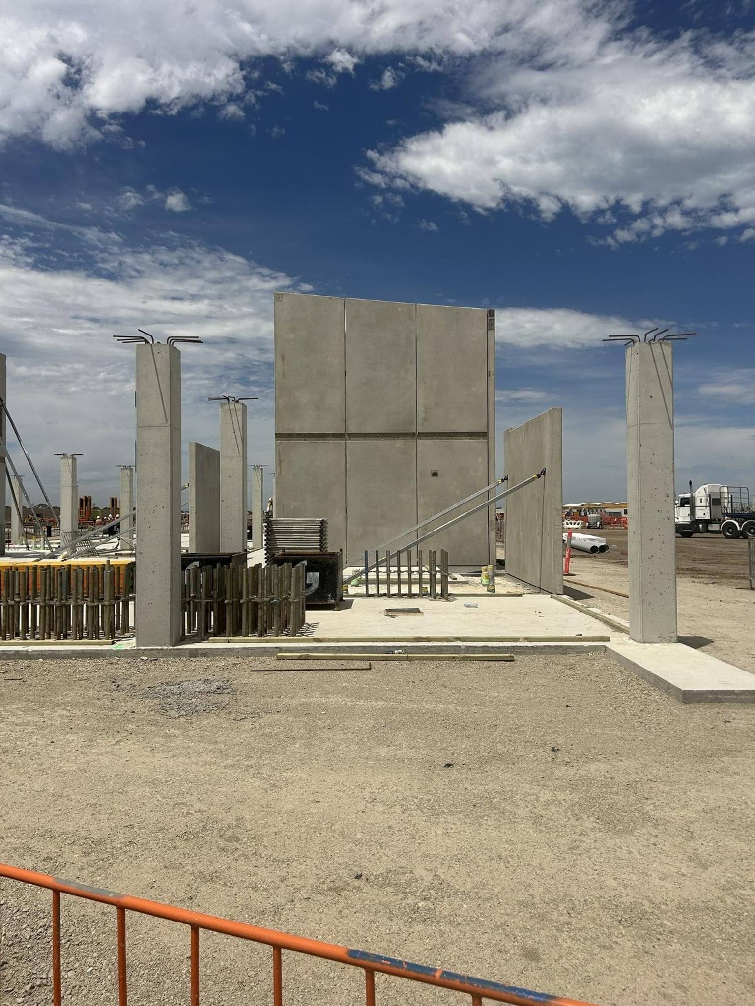 A construction site with large concrete wall panels and upright columns installed on a foundation slab.