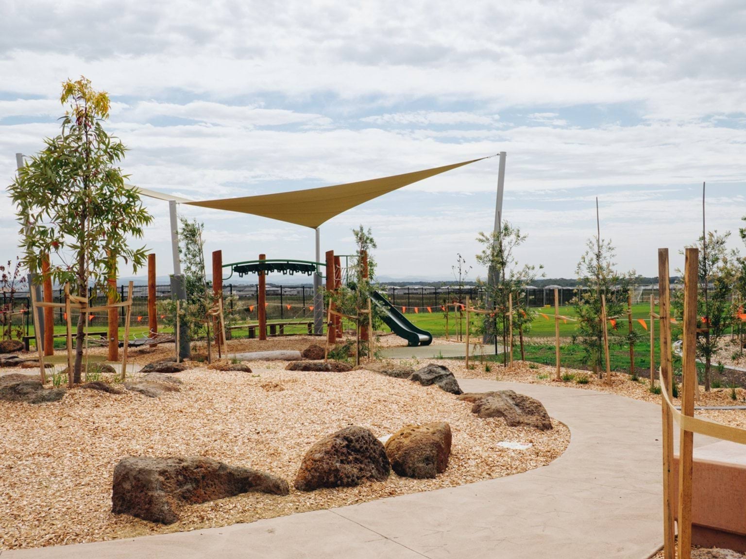 Outdoor play area with shade sail, slide structure, concrete paths and newly planted landscape beds