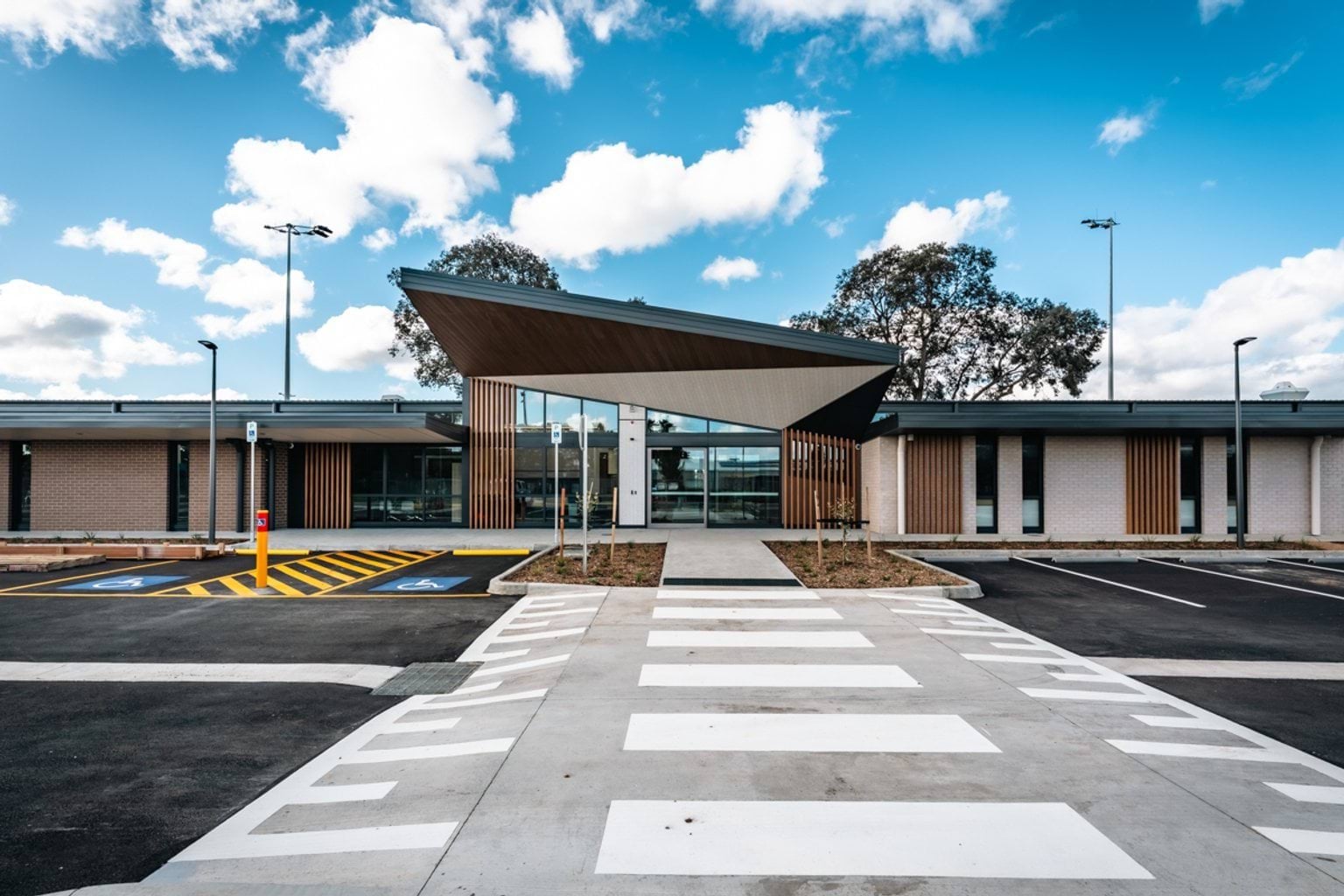 The exterior of a modern kindergarten building with a large angled roof over the entrance and a wide pedestrian crossing leading to the front door.