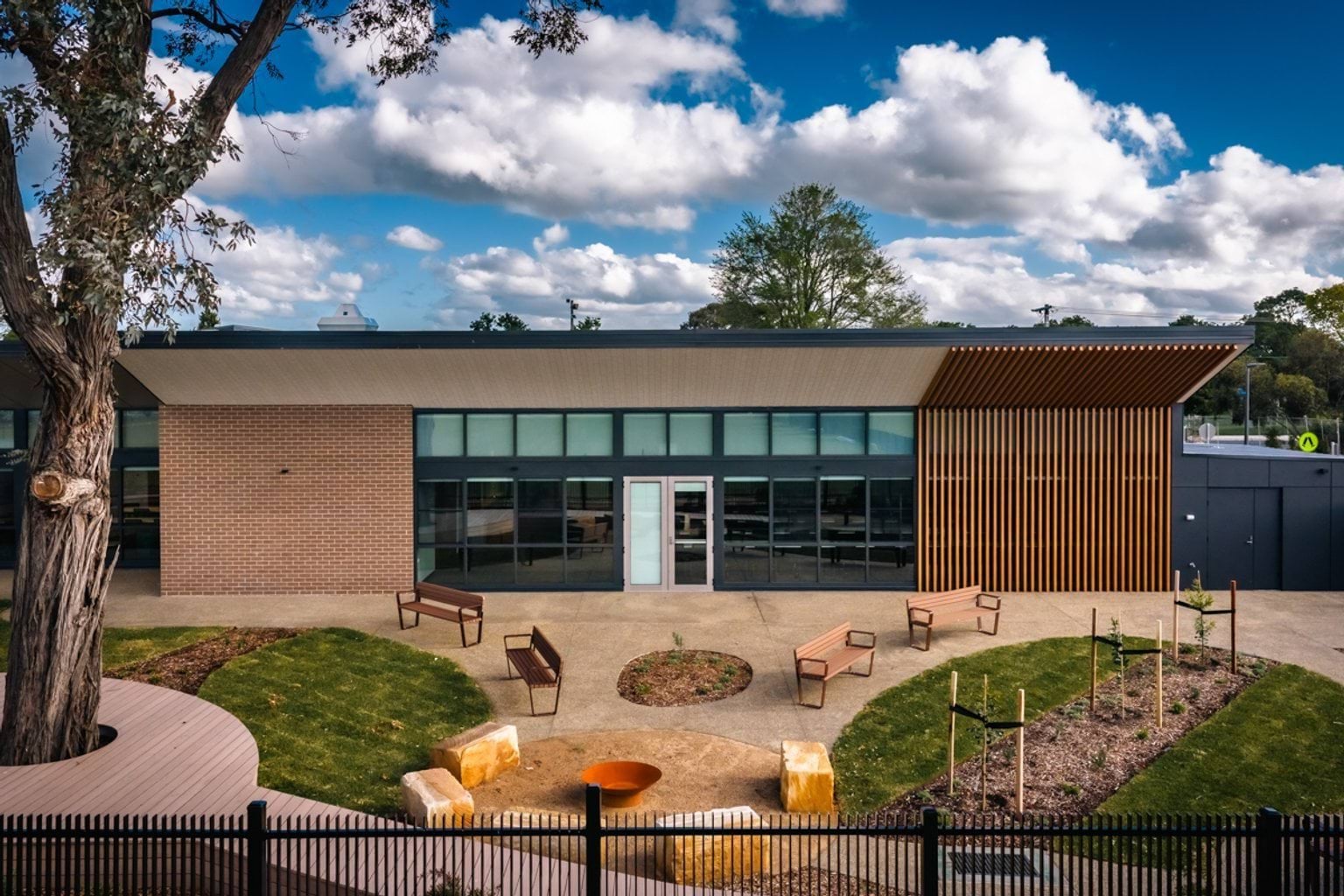 An outdoor courtyard with landscaped garden beds, curved seating, stone elements, and a brick kindergarten building behind.