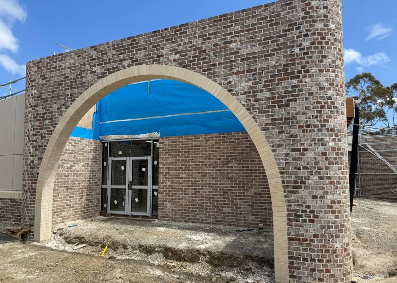 A large brick archway framing an unfinished entrance, with blue weatherproof sheeting covering the structure above.