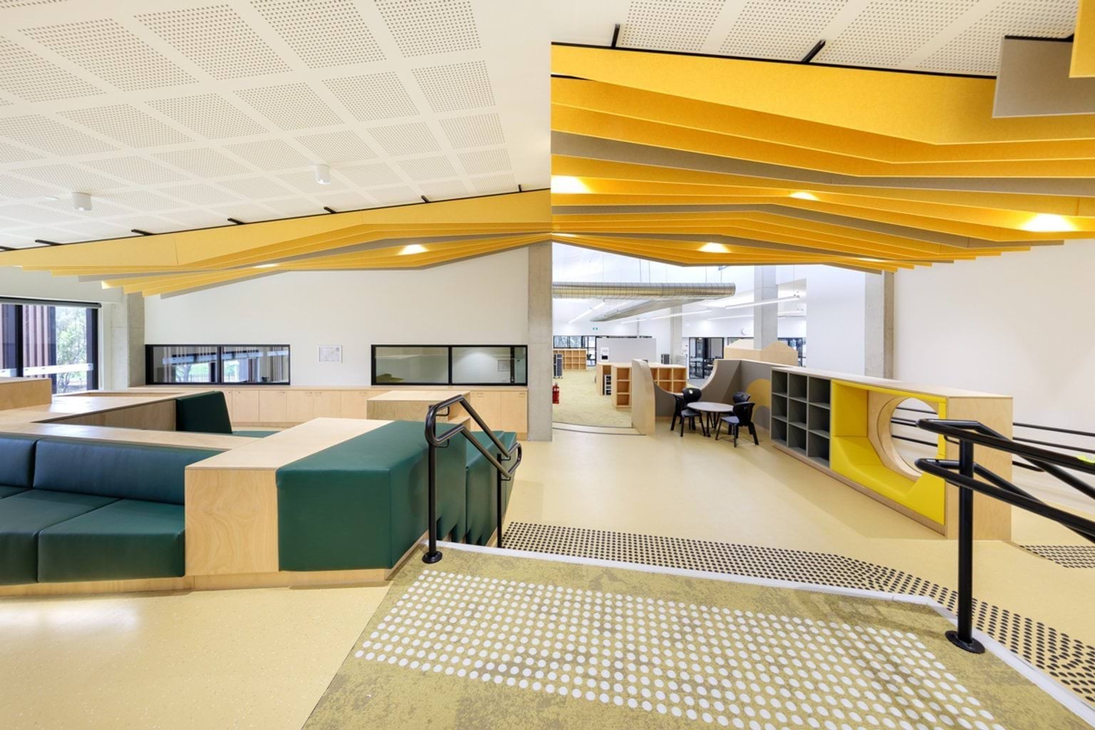 Learning commons with tiered seating, timber and upholstered joinery and yellow acoustic ceiling panels.