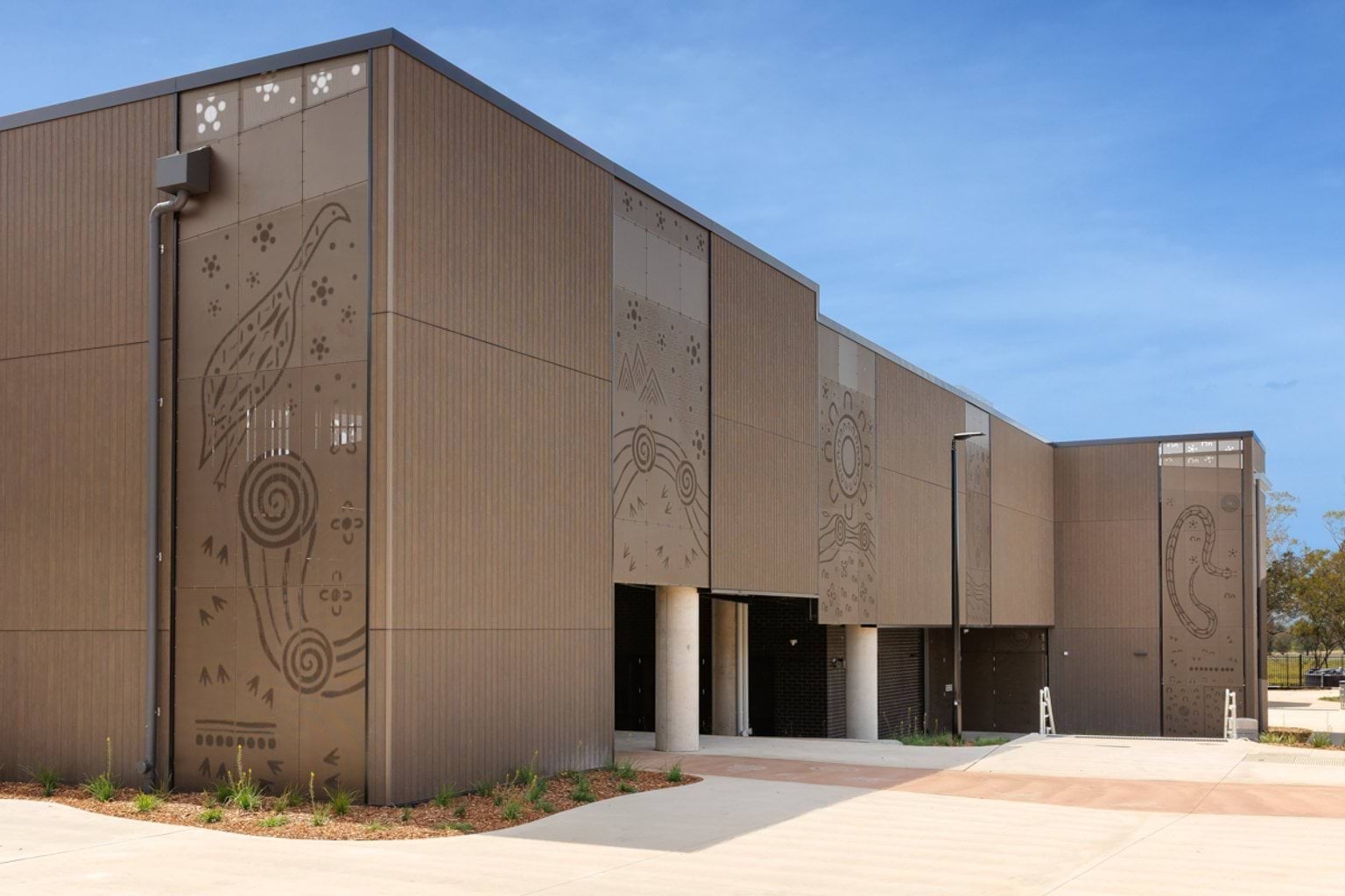 Exterior of a modern school building with vertical cladding and large decorative panels featuring Indigenous-inspired artwork.