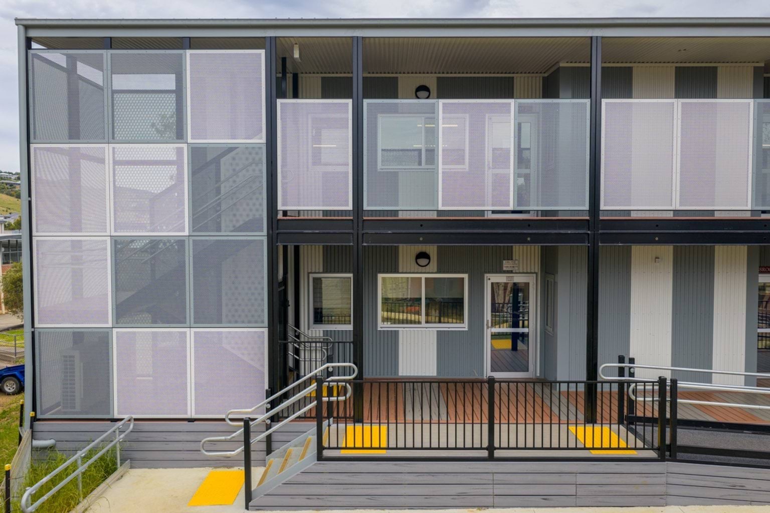 The exterior of a two‑storey modular school building with screened balconies, ramps, and contrasting grey wall panels.