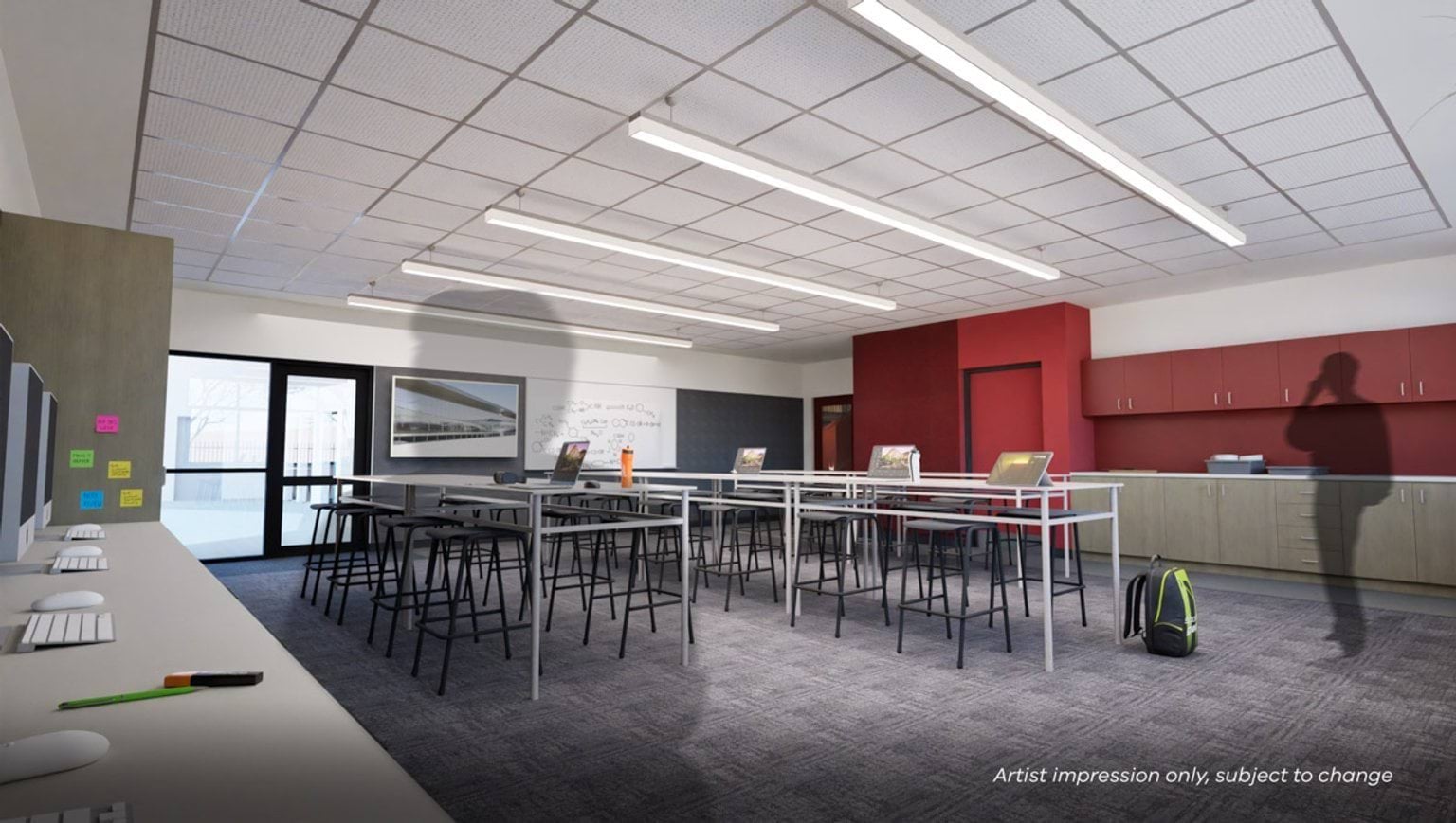 Artist’s impression of a contemporary visual communications classroom with high collaborative tables, desktop computers, red feature wall, and built-in storage cabinetry.