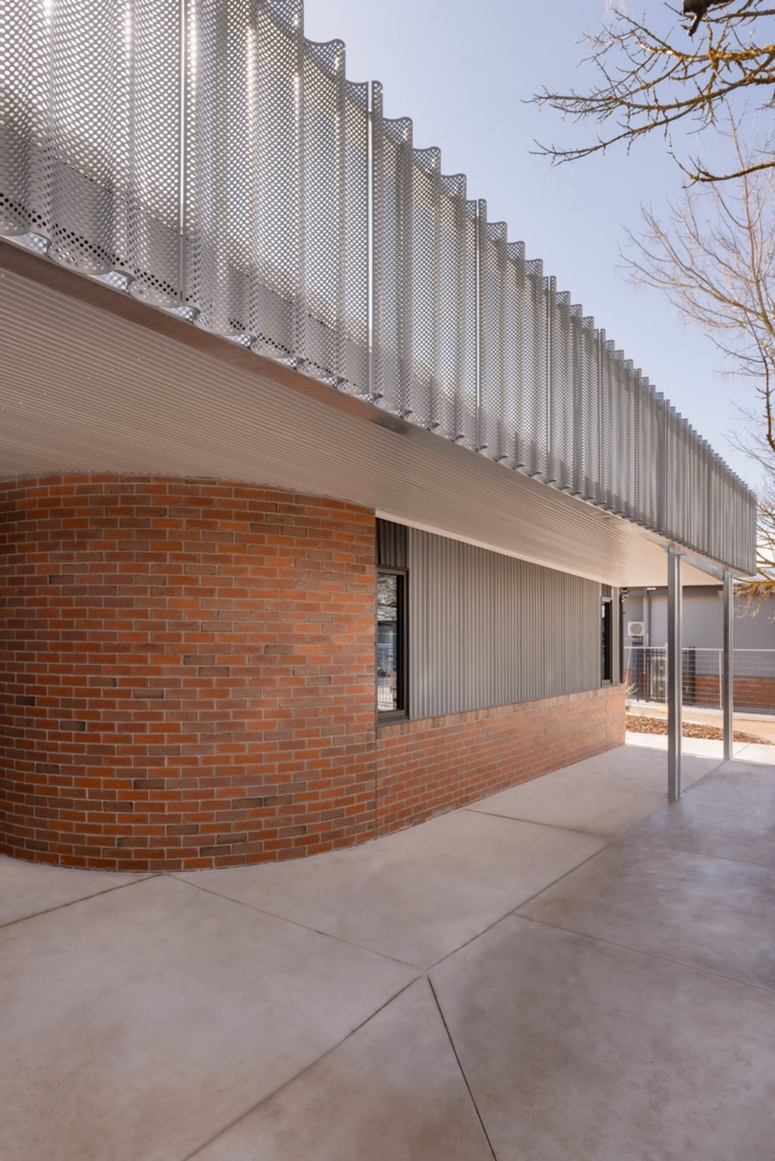 The exterior of a school building with curved brick walls, grey metal panels, and a perforated metal screen above a covered walkway.
