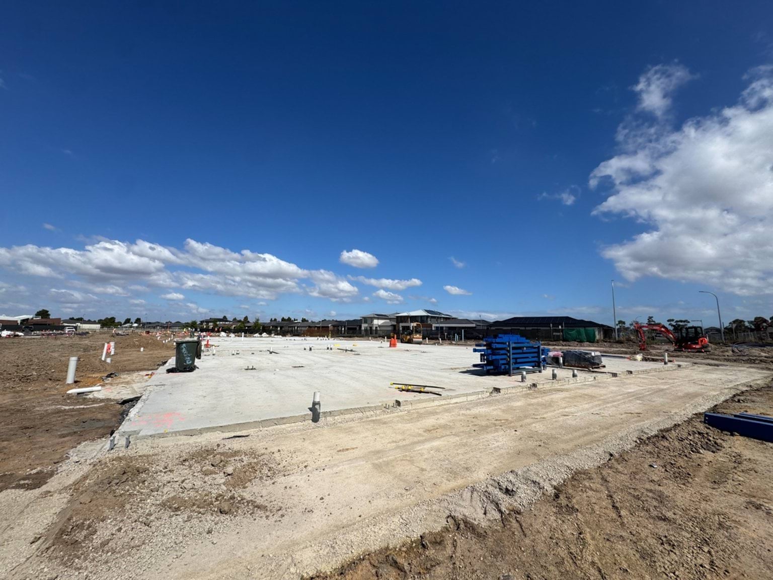 A wide concrete slab newly poured on a school construction site, with tools and materials stacked nearby.