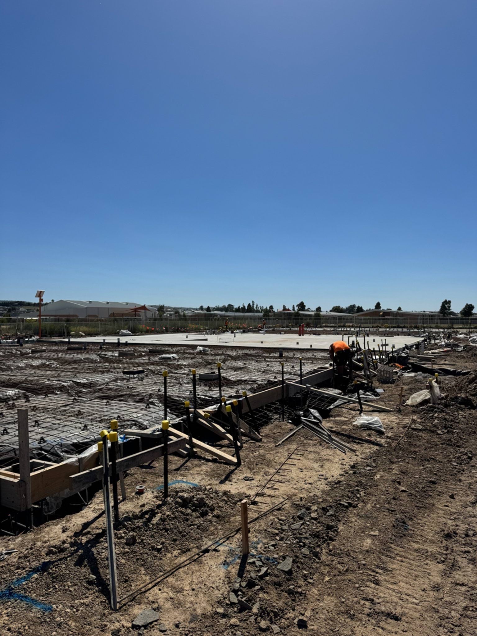 Workers preparing formwork and steel reinforcement for a concrete slab across a large building site.