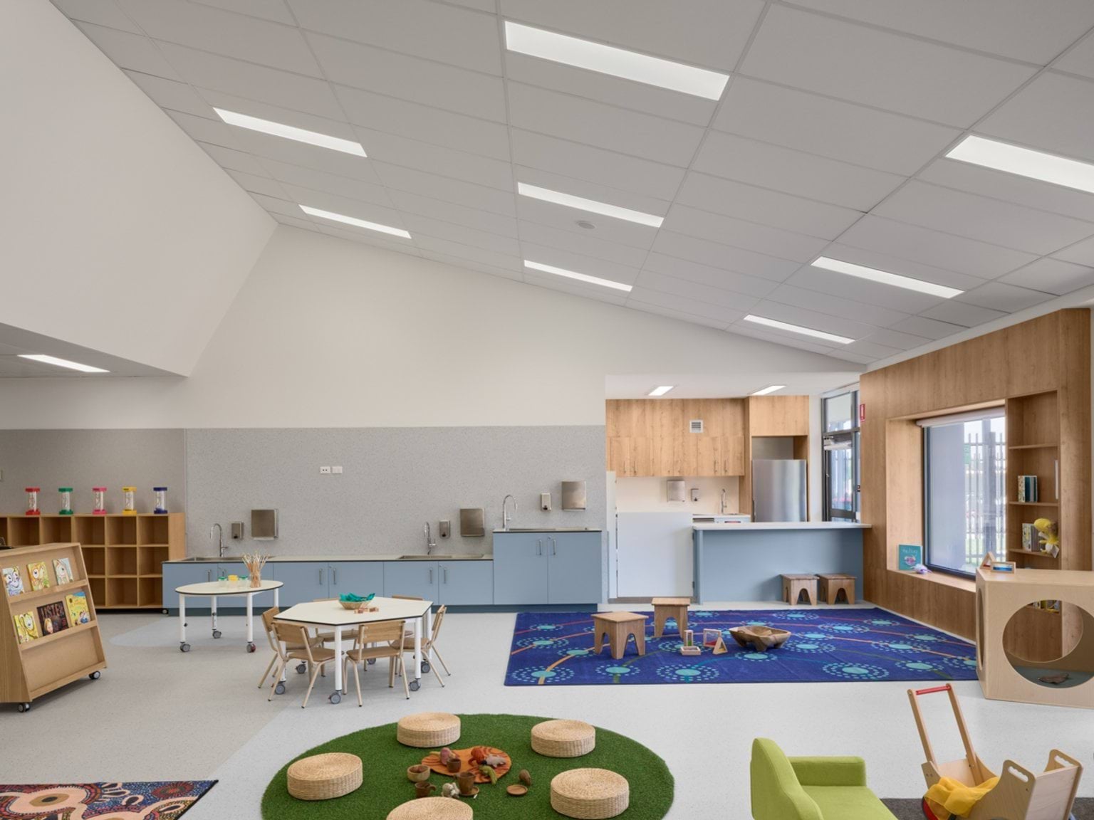 A spacious early learning room with creative play zones, child‑sized furniture, a kitchen area, and colourful rugs.