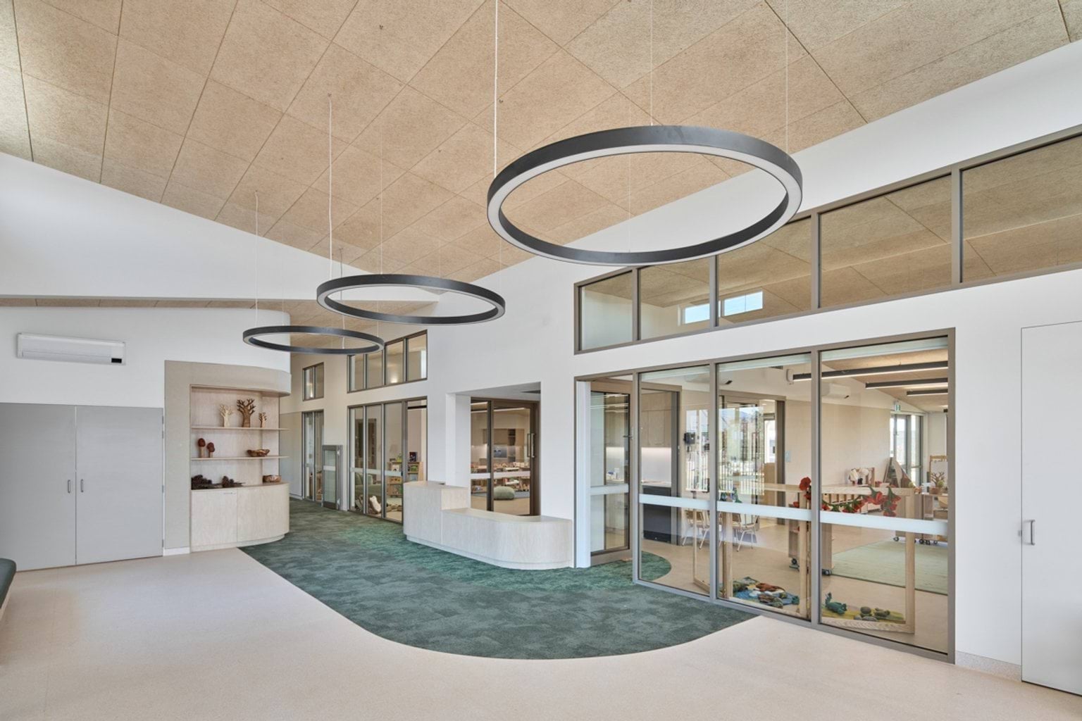 A reception and circulation space with large circular light fittings, glass-fronted rooms, and built-in shelving and joinery.