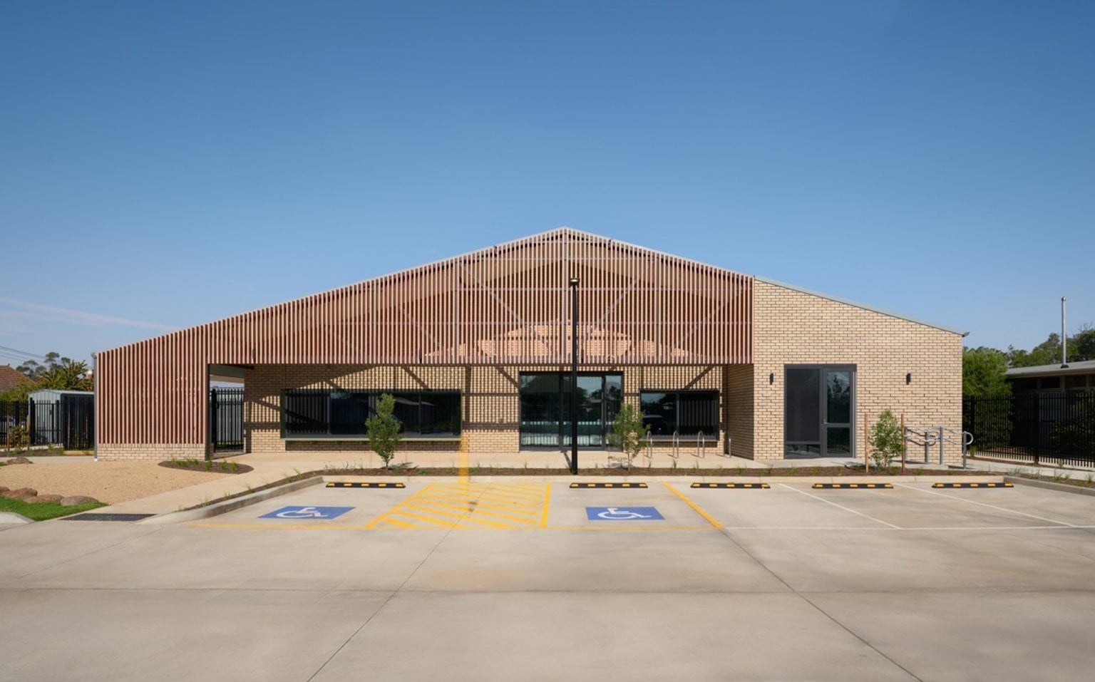 The front exterior of an early learning centre with brick walls, a slatted timber façade, large windows, and accessible parking spaces.